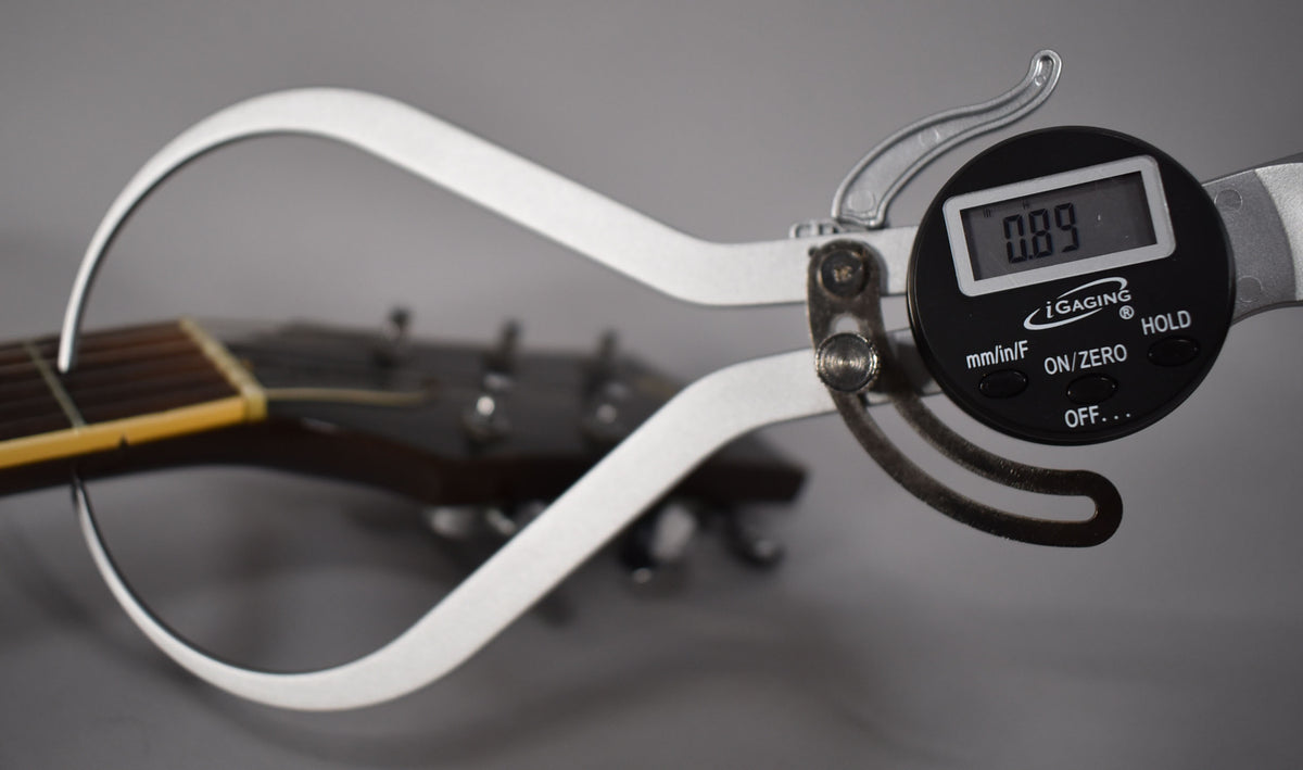 A digital caliper measures the dark walnut guitar's nut, showing a reading of 0.89.
