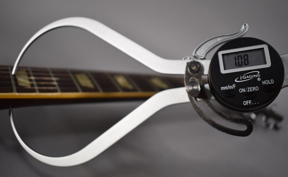 A digital caliper measures the guitar's dark fretboard, showing 1.08mm, with trapezoid inlays visible.