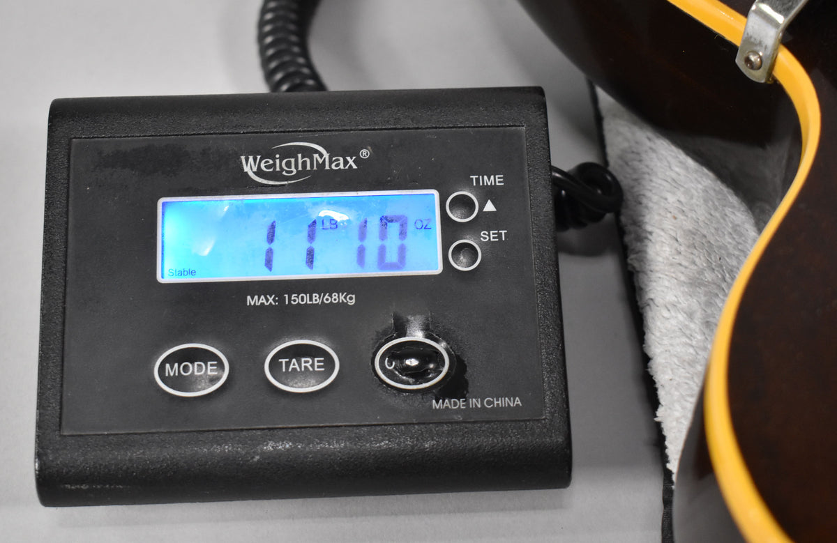 A black digital scale displays "11 LB 10 OZ" next to the dark walnut body and cream binding of the guitar.