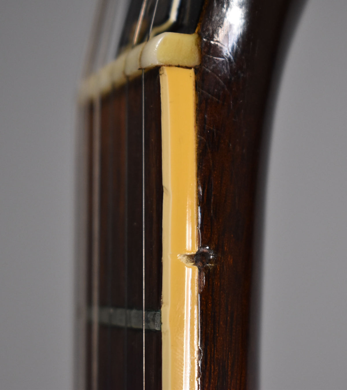 Close-up of the dark walnut neck and binding, showing a chip in the binding near the nut and light finish wear.