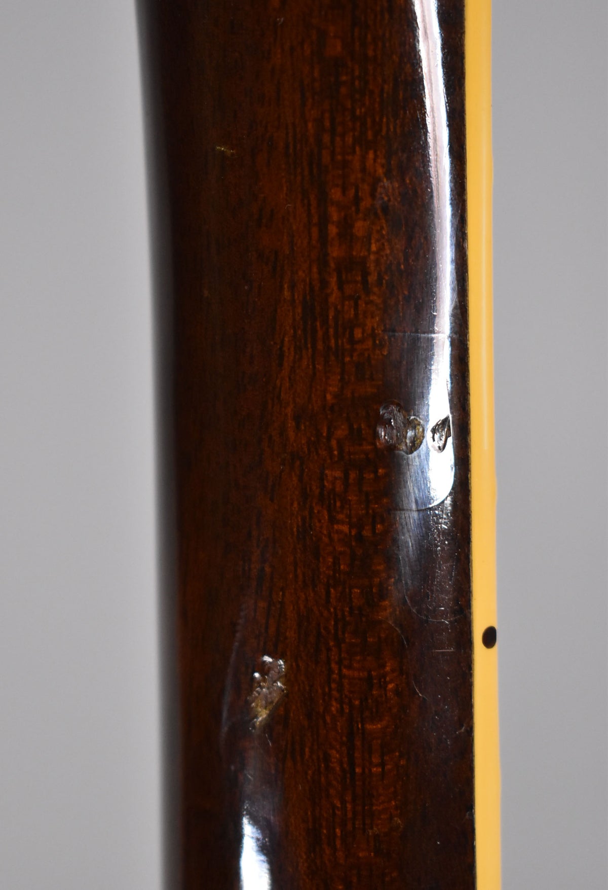 Close-up of the dark walnut neck, showing two deep dings and a smaller scratch, with cream binding and a black side dot.