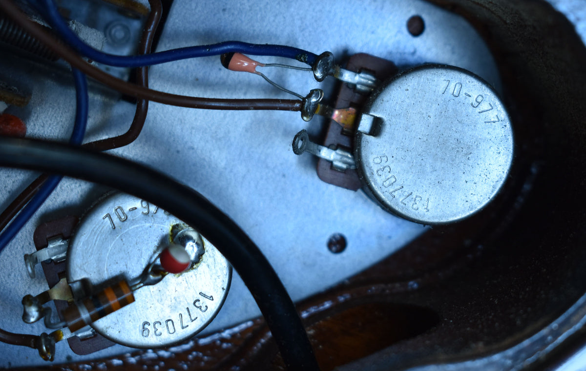 Close-up of the guitar's internal electronics, showing two silver potentiometers with visible numbers, wires, and a resistor.