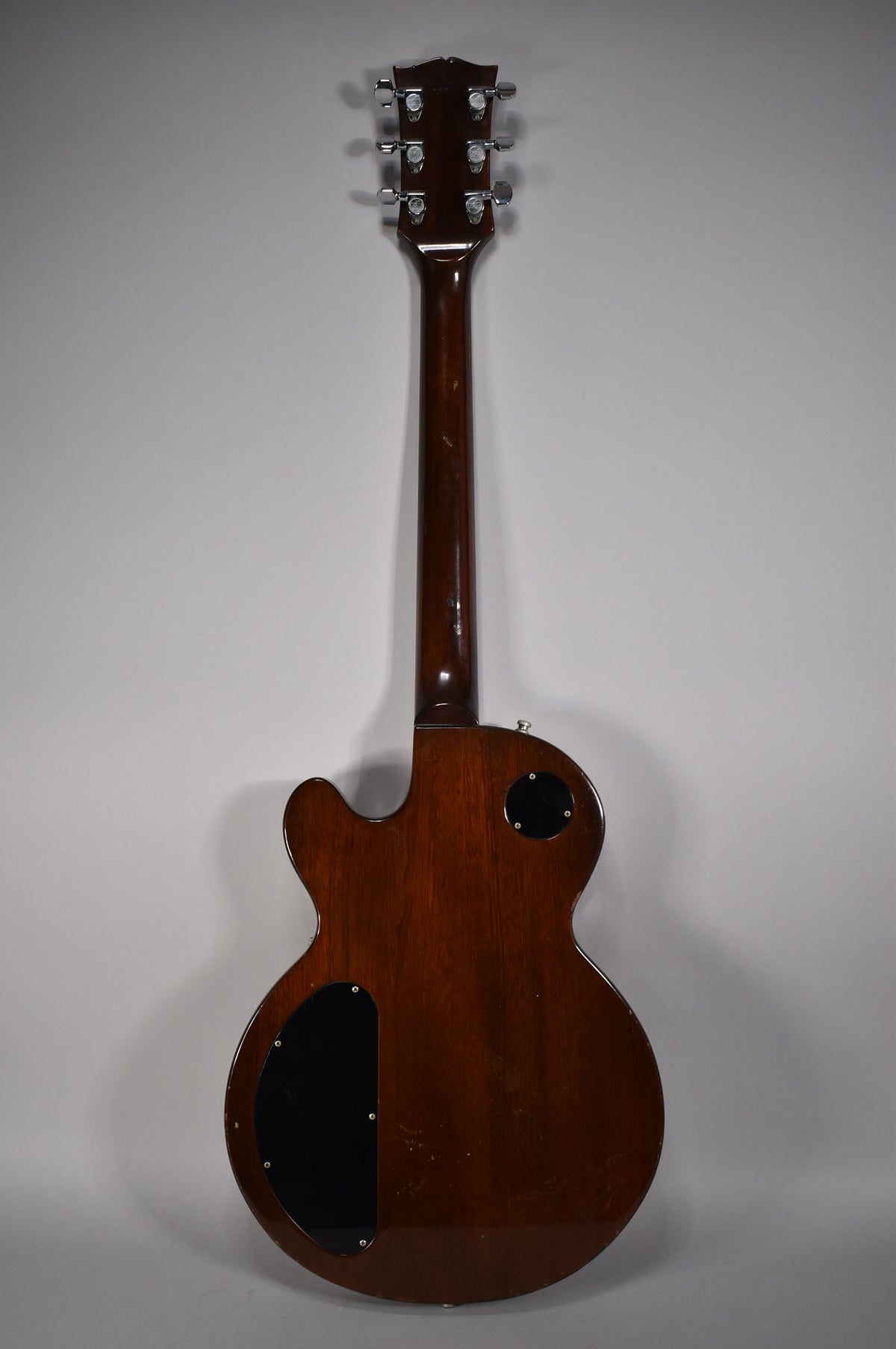 The back of a dark walnut Les Paul, showing the headstock, neck, and body with two black control cavity covers.