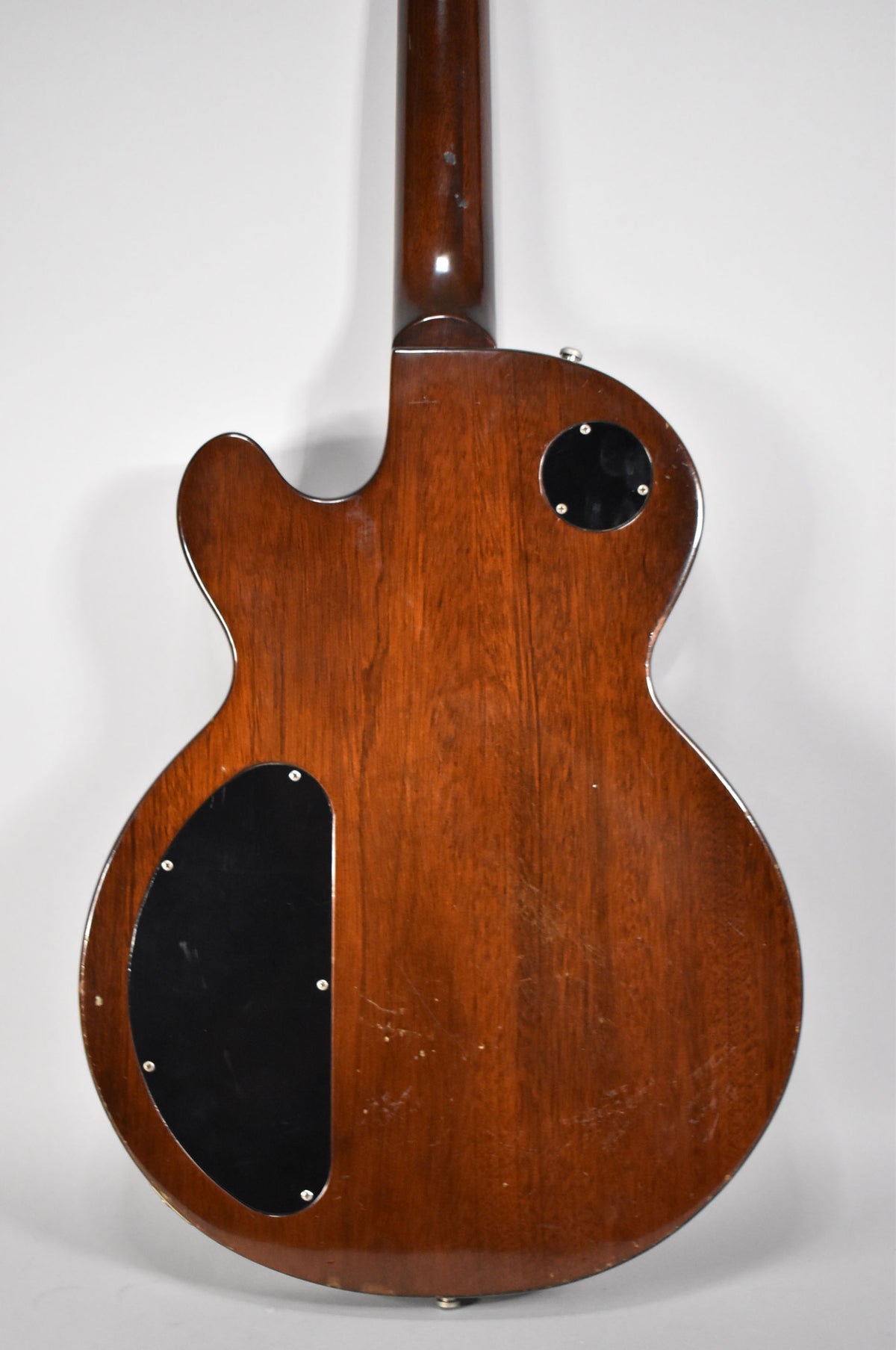 The back of a dark walnut guitar with two black control cavity covers, showing light scratches and wear on the body and neck.