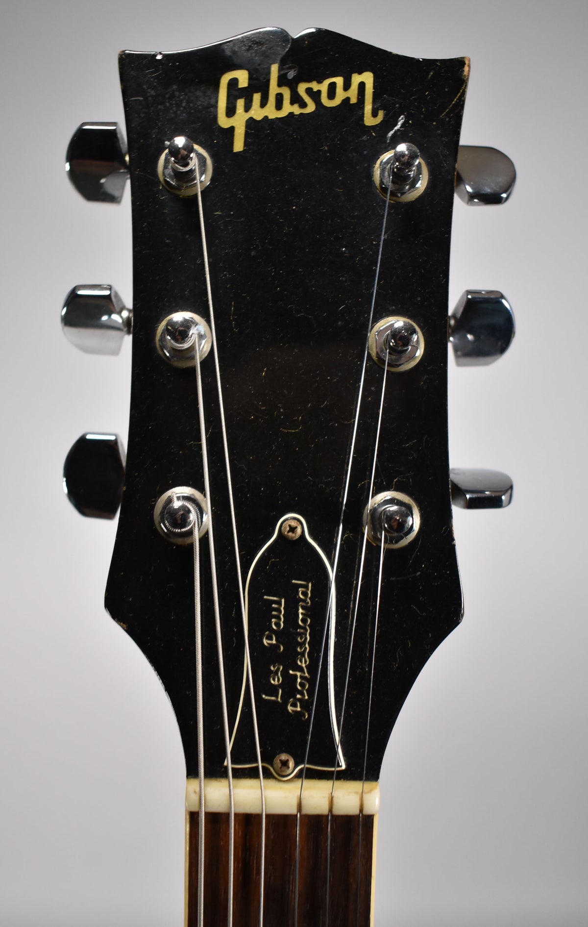 Close-up of the black headstock with chrome tuners, showing a white truss rod cover and some finish wear on the top edge.