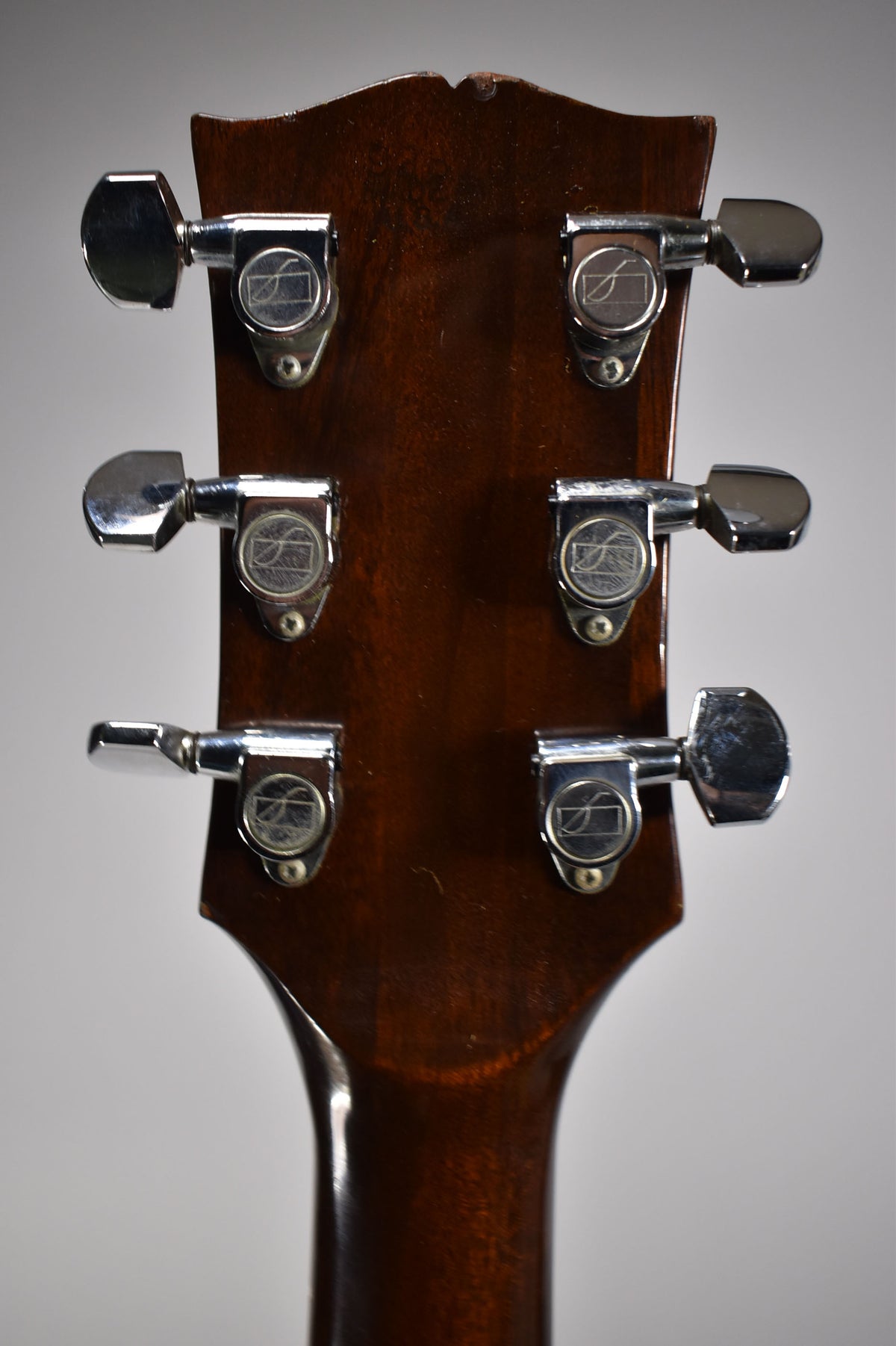 The guitar's dark walnut headstock, viewed from the back, shows six chrome tuners with visible wear and a small chip at the top.