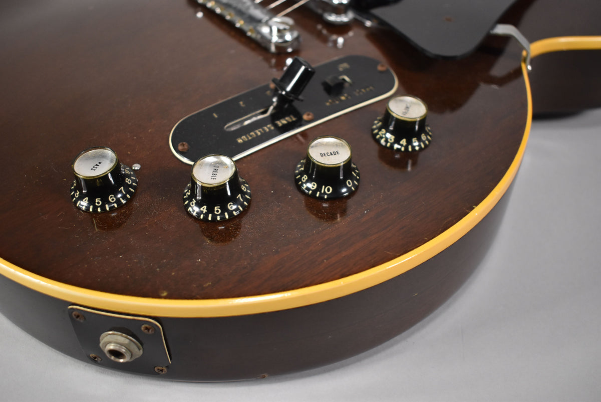 Close-up of the dark walnut body, showing four black control knobs, a tone selector switch, and the output jack with some wear.
