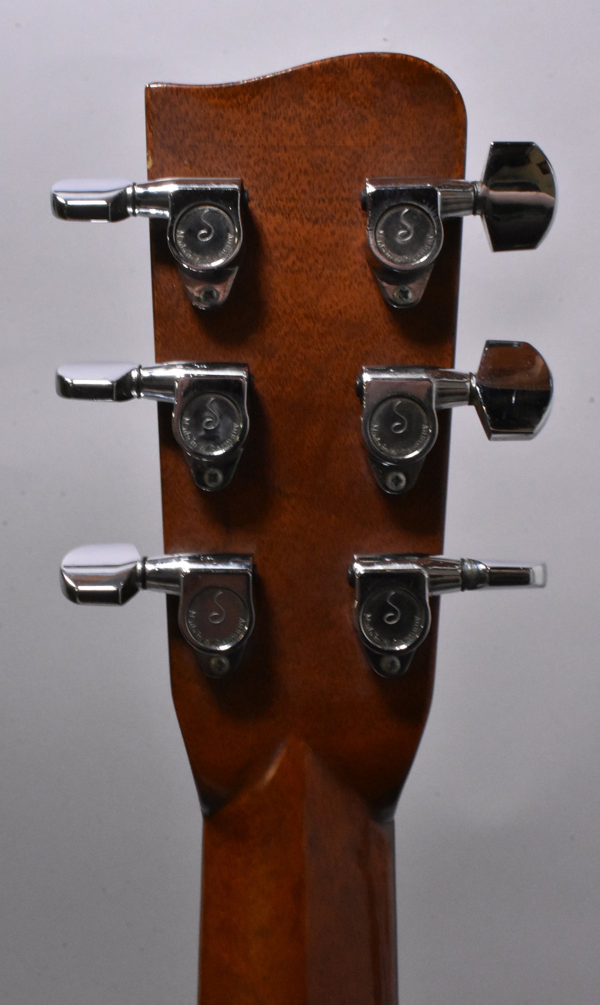 The back of the guitar's headstock, showing six chrome tuners with white buttons on a dark brown wood finish.