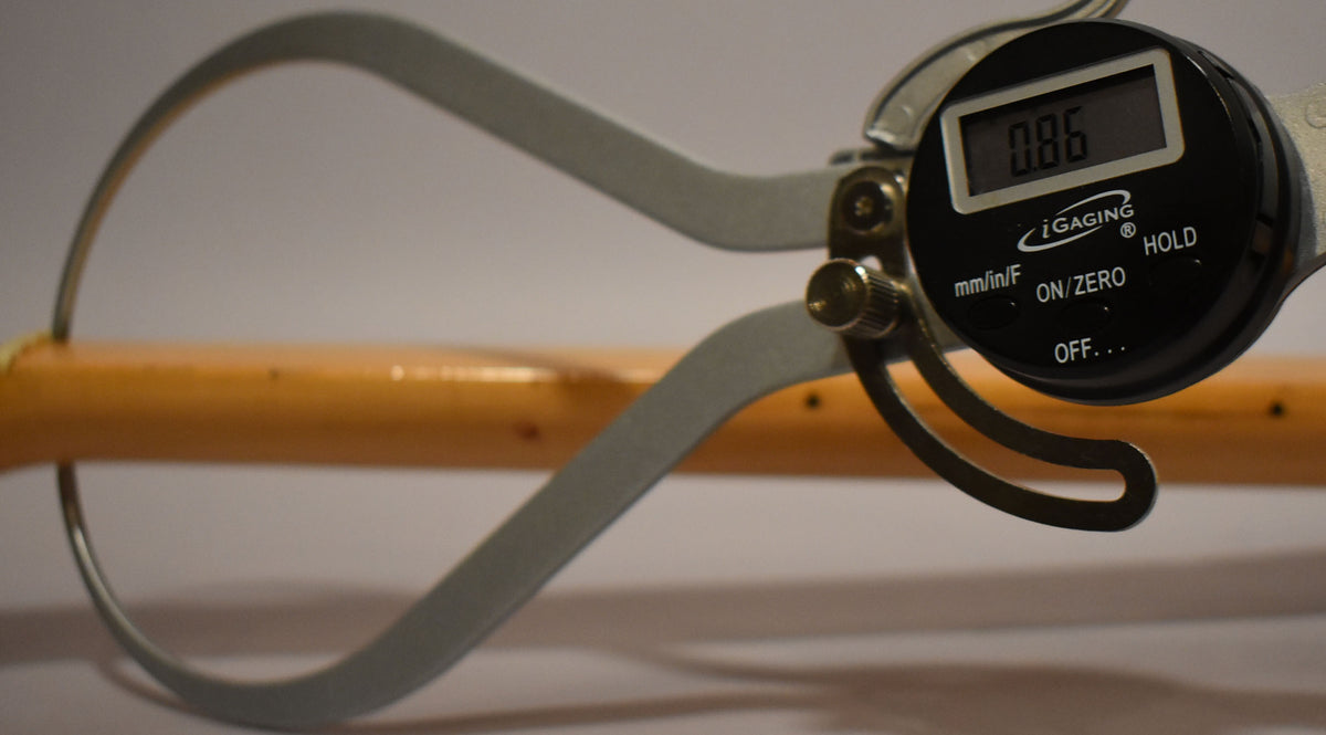 A digital caliper measures the maple neck, displaying "0.86" on its screen, with light wear visible on the neck's finish.