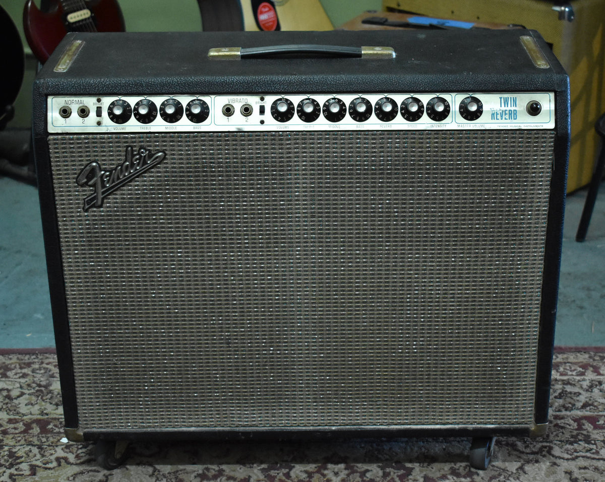 Front view of a black combo amp with a silver grille cloth, a chrome control panel with 12 black knobs, and a top handle.