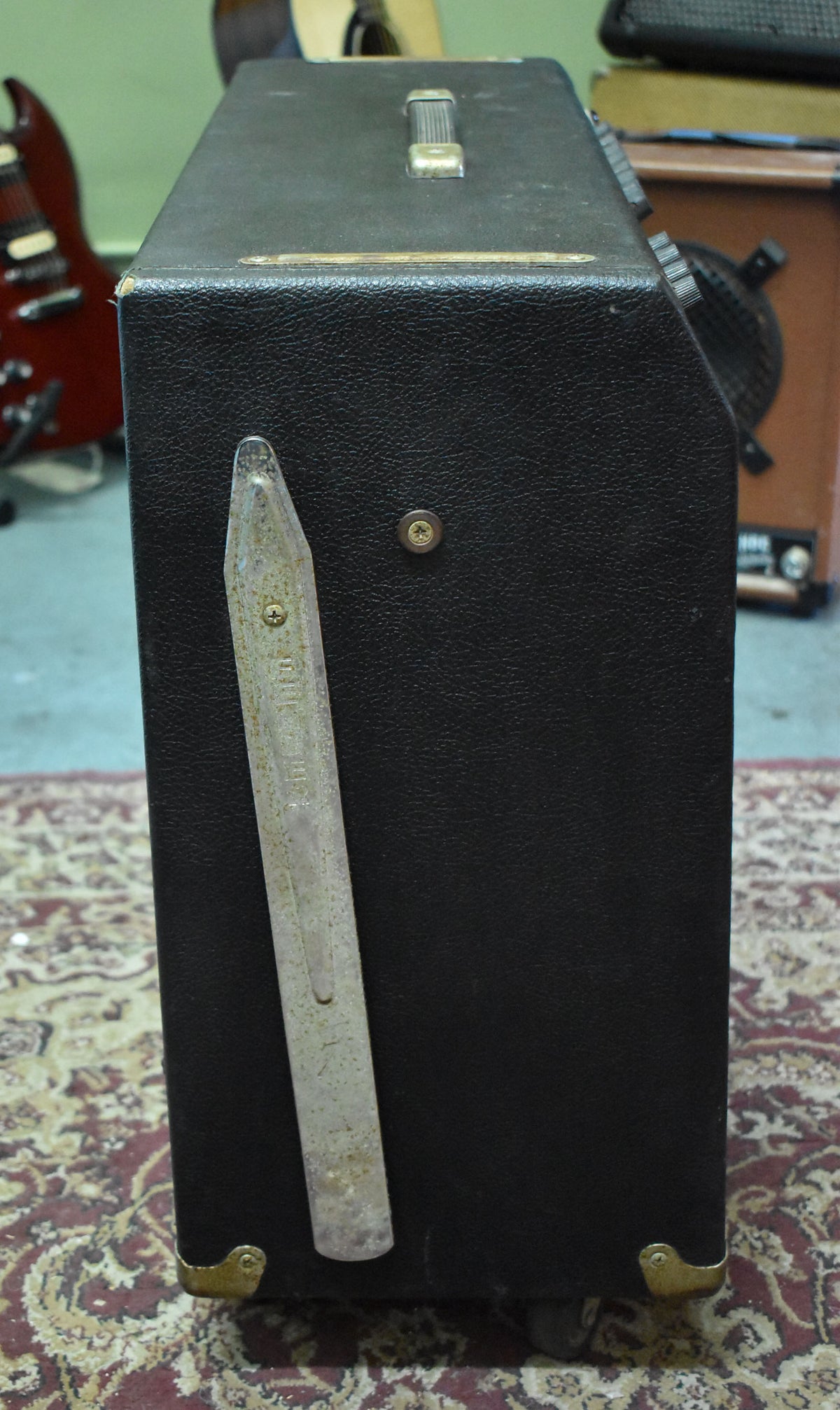 Right side of the black tolex amp, showing a worn chrome tilt-back leg, a metal handle, and brass corner protectors.