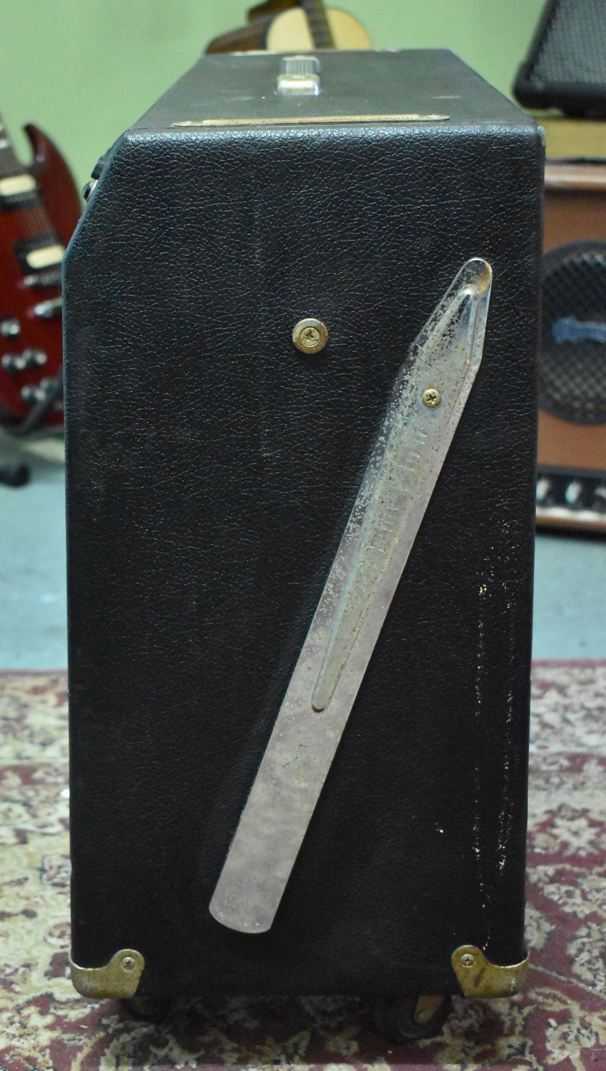 Right side of the black tolex amp, showing a worn, tarnished tilt-back leg, brass corner protectors, and casters.