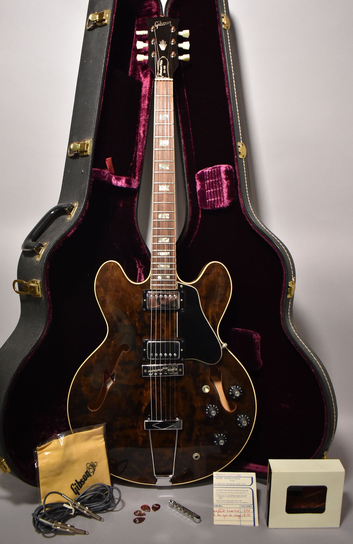 Full-length view of a dark walnut semi-hollowbody guitar with f-holes, chrome hardware, and a black pickguard, in its open purple-lined case.