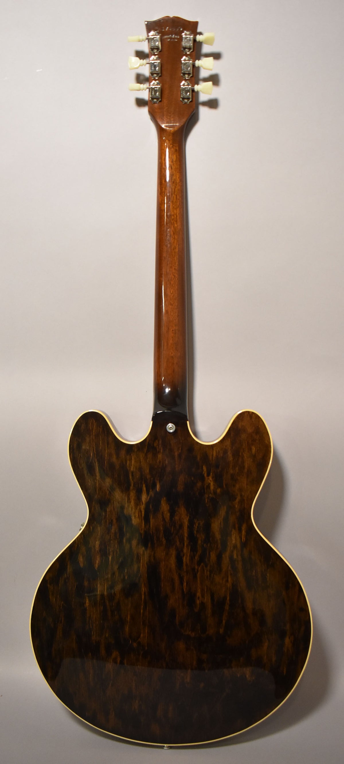 The guitar's back, neck, and headstock are visible, showing a dark walnut finish with prominent wood grain and light binding.