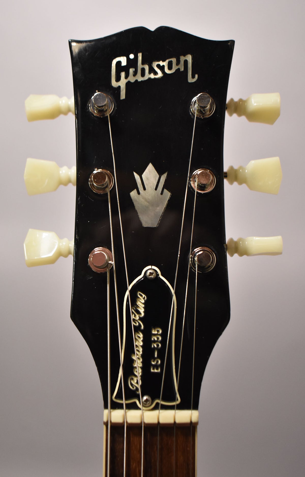 Close-up of the black headstock with mother-of-pearl inlays, six cream tuning pegs, and light finish checking.