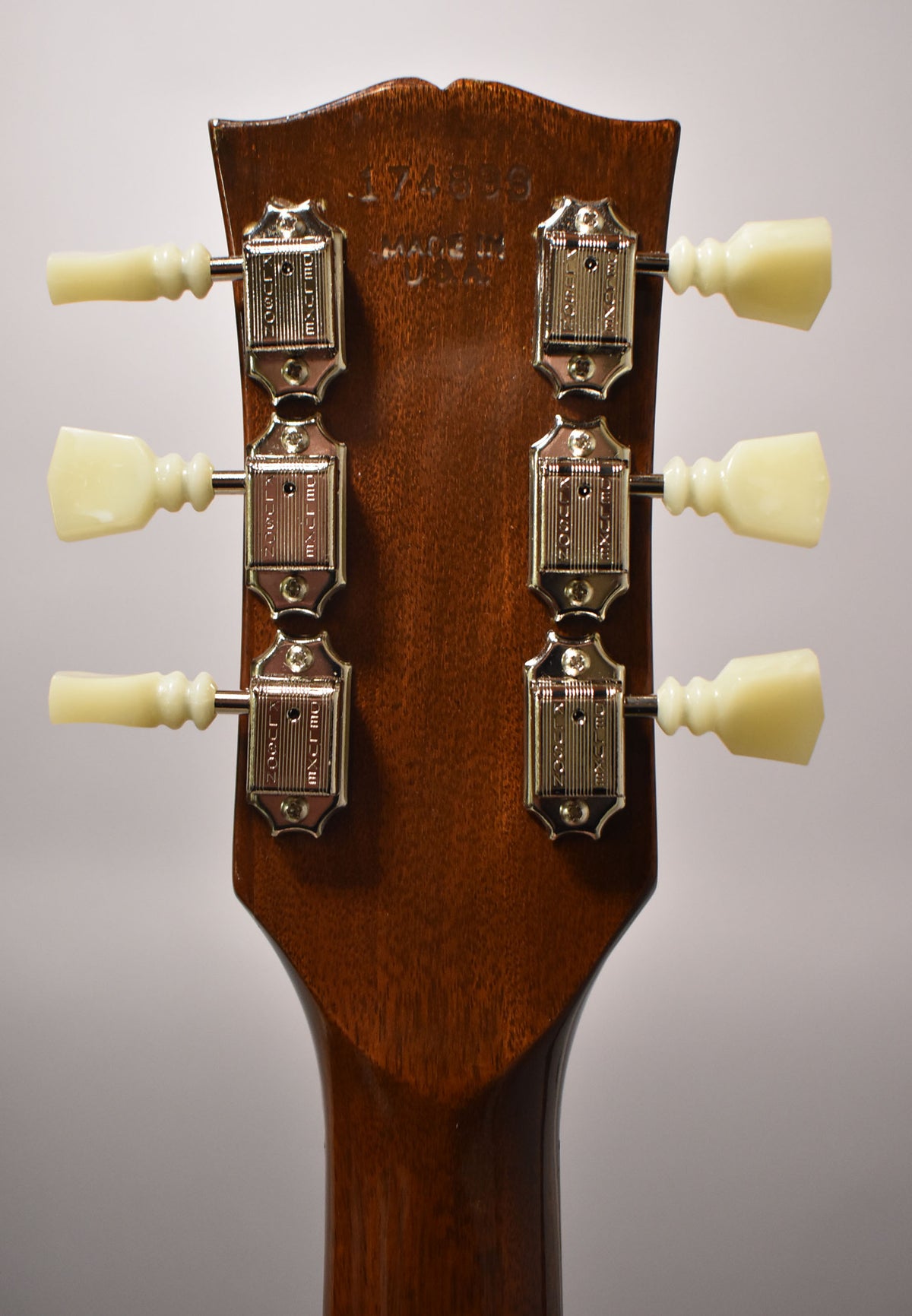 The guitar's walnut-finished headstock, viewed from the rear, shows six chrome tuners with cream plastic tulip buttons.
