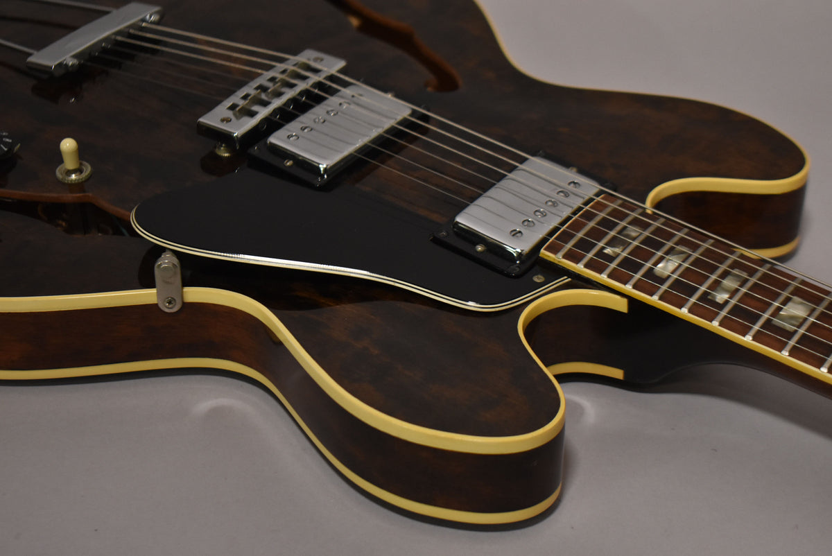 Close-up of a dark walnut semi-hollowbody electric guitar, showing the lower bout, black pickguard, two chrome humbuckers, and part of the fretboard.