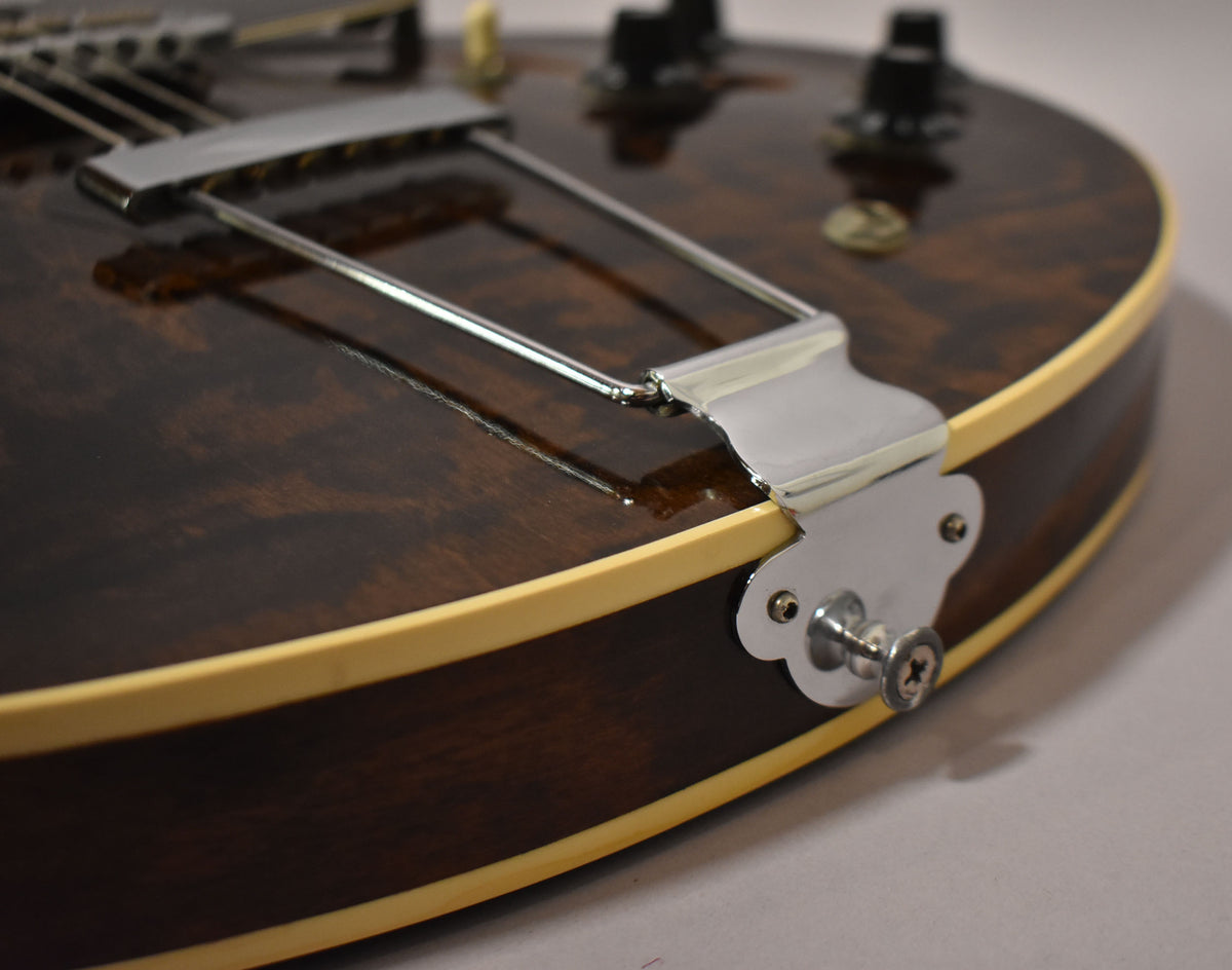 Close-up of the guitar's lower bout, showing the dark walnut finish, cream binding, chrome trapeze tailpiece, and endpin jack.