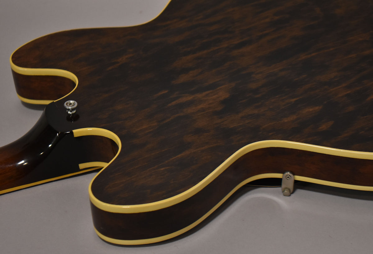 The back of a dark walnut hollow-body guitar, showing the lower bout, cutaway, and neck heel with a strap button.