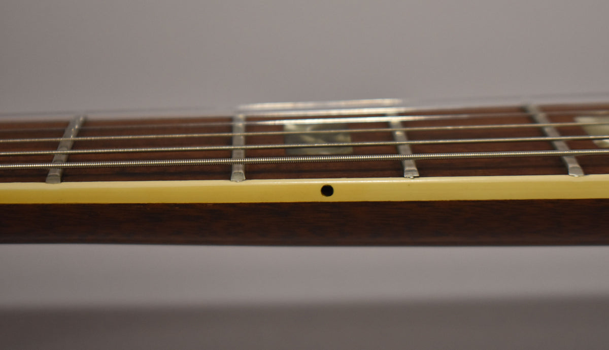 Close-up of the guitar's dark fretboard and strings, showing a cream binding with a single black dot marker at the 7th fret.