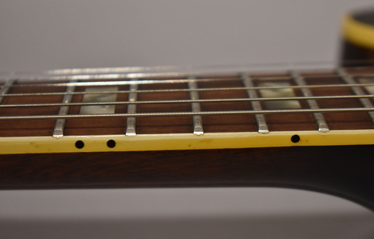 Close-up of the dark rosewood fretboard with block inlays, showing light wear on the frets and cream binding with side dots.