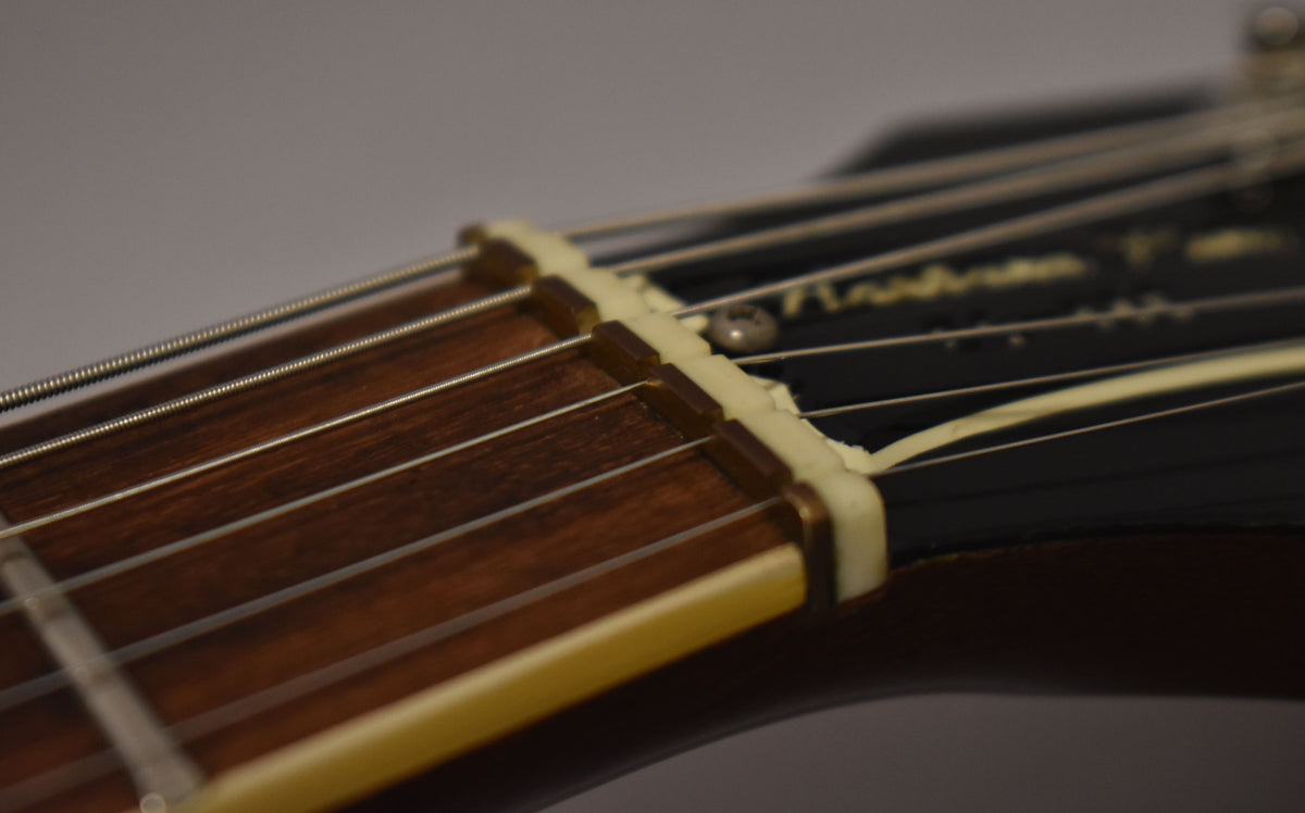 Close-up of the nut and first frets, showing a dark rosewood fretboard, cream binding, and a chipped, aged cream nut.