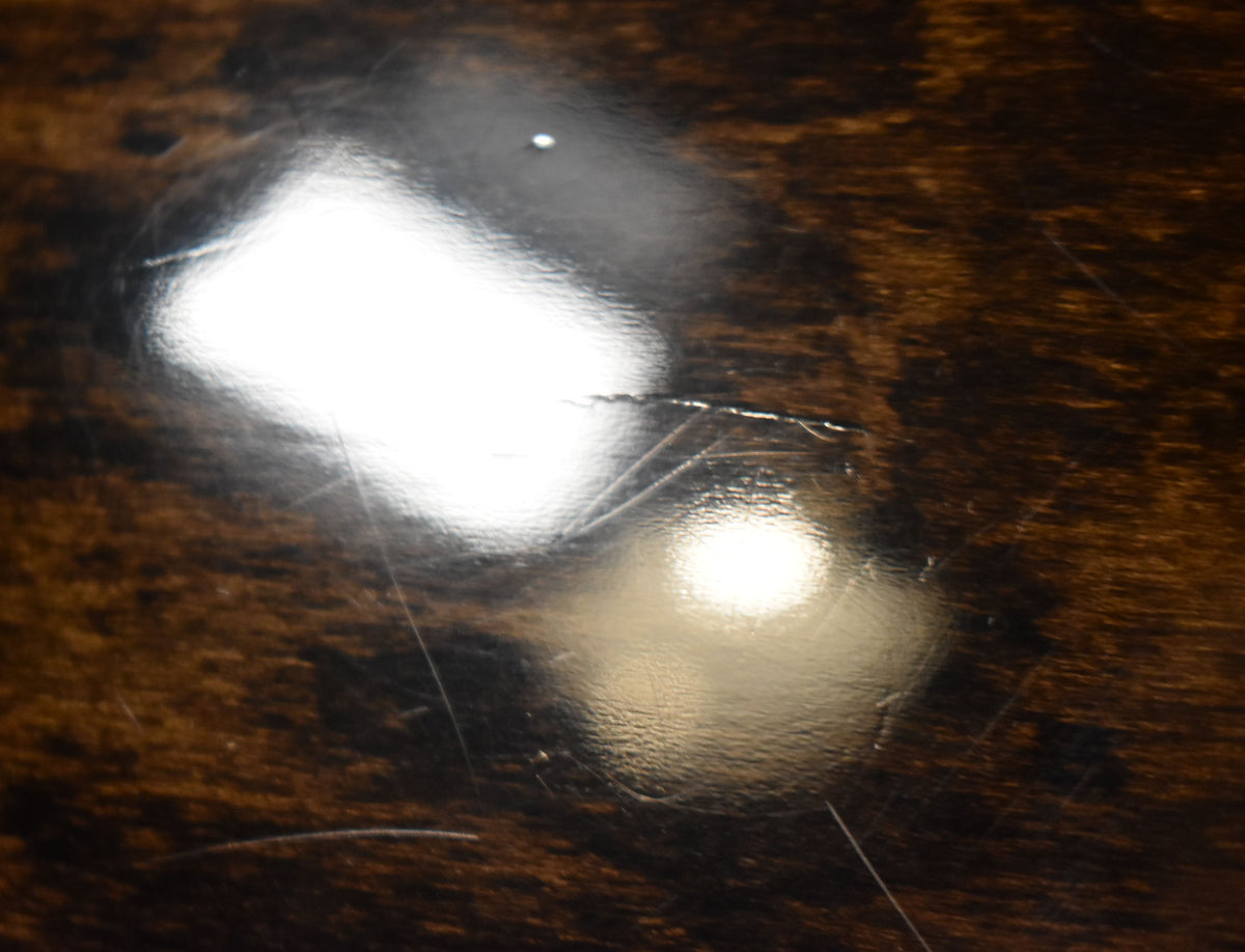 Close-up of the guitar's glossy walnut finish, showing light surface scratches and a small crack in the lacquer near a bright reflection.