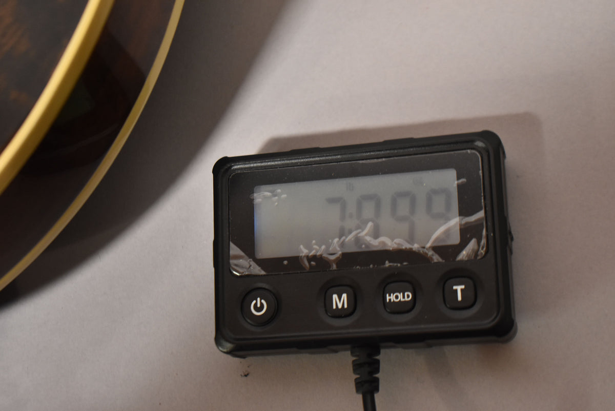 Close-up of a digital scale displaying "7.099" with a cracked screen, next to the dark walnut body binding of the guitar.