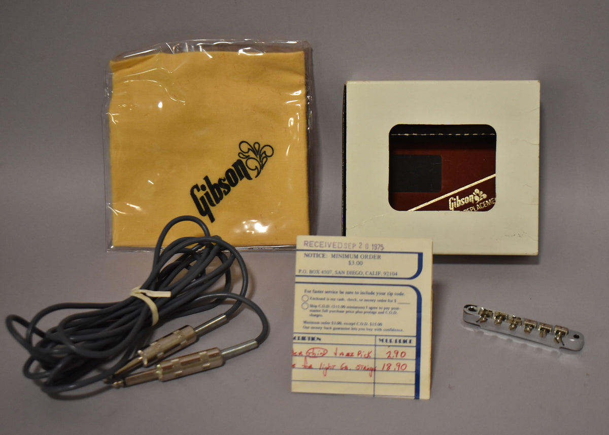 Included accessories: a coiled gray cable, a yellow cloth in plastic, a small white box, a receipt, and a chrome bridge.