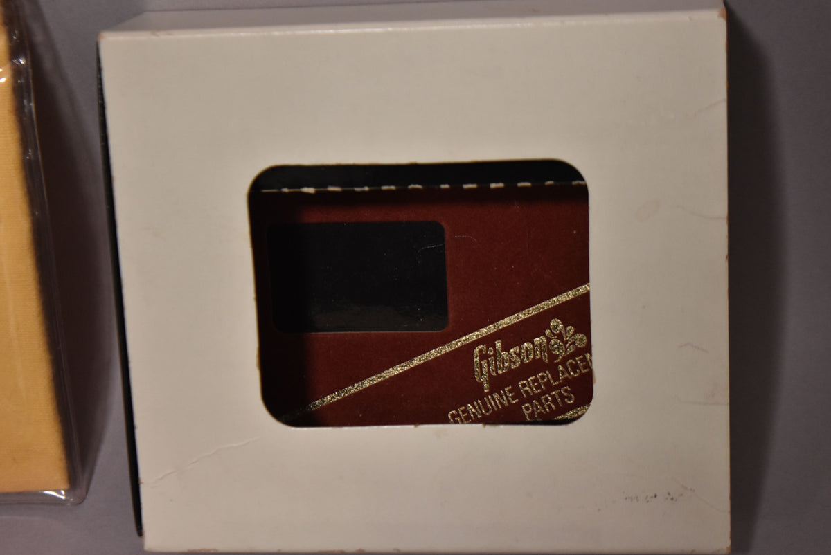 A white cardboard box with a rectangular cutout revealing a dark red "Gibson Genuine Replacement Parts" label.