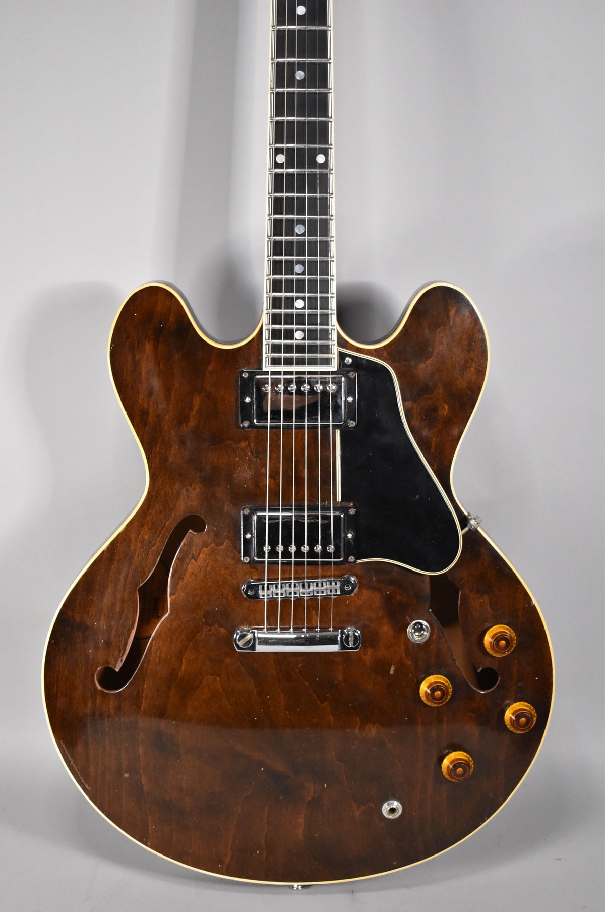 Full-frame, dark walnut semi-hollowbody guitar with f-holes, two humbuckers, black pickguard, and four amber control knobs.