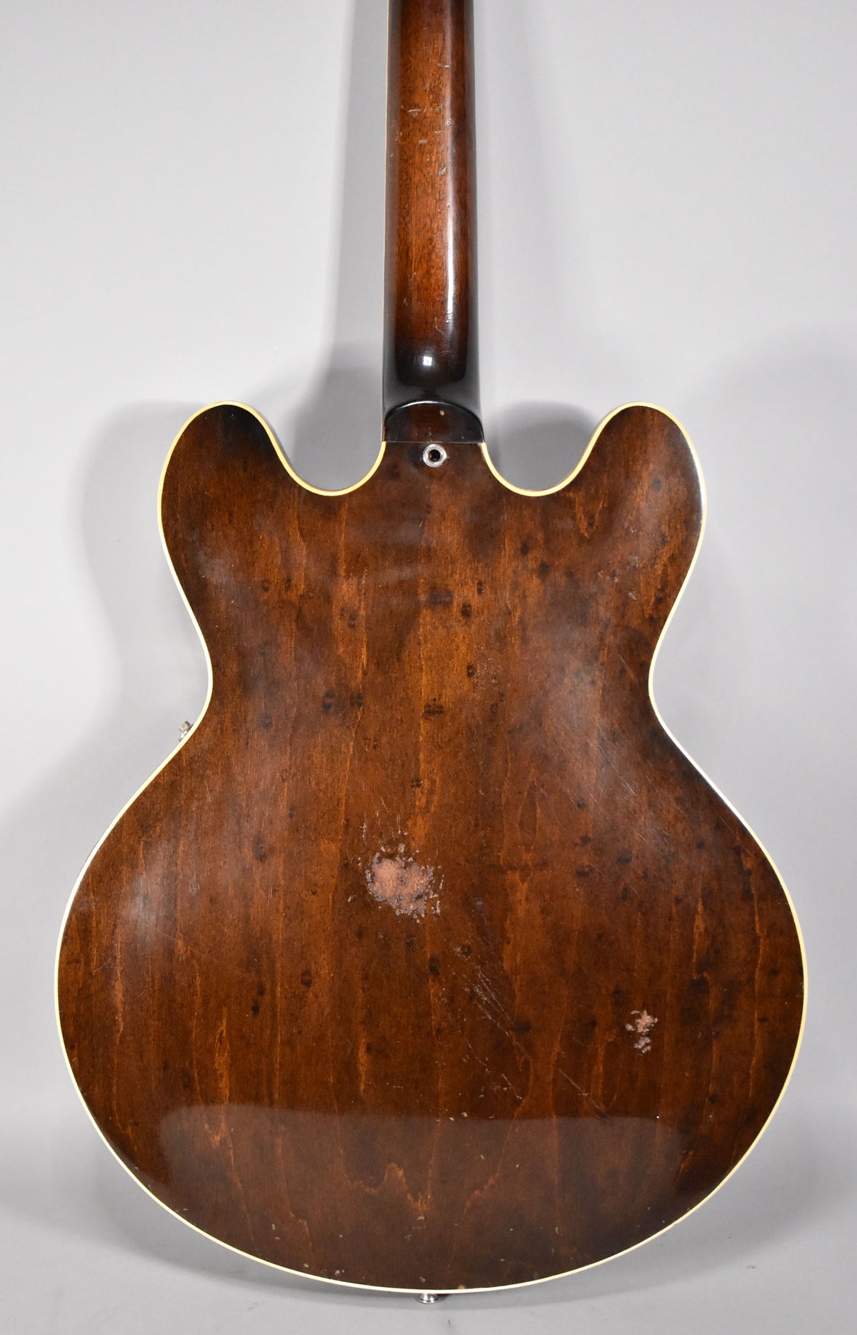 Full rear view of a dark walnut hollow-body guitar with heavy finish wear, scratches, and a large worn patch on the lower bout.