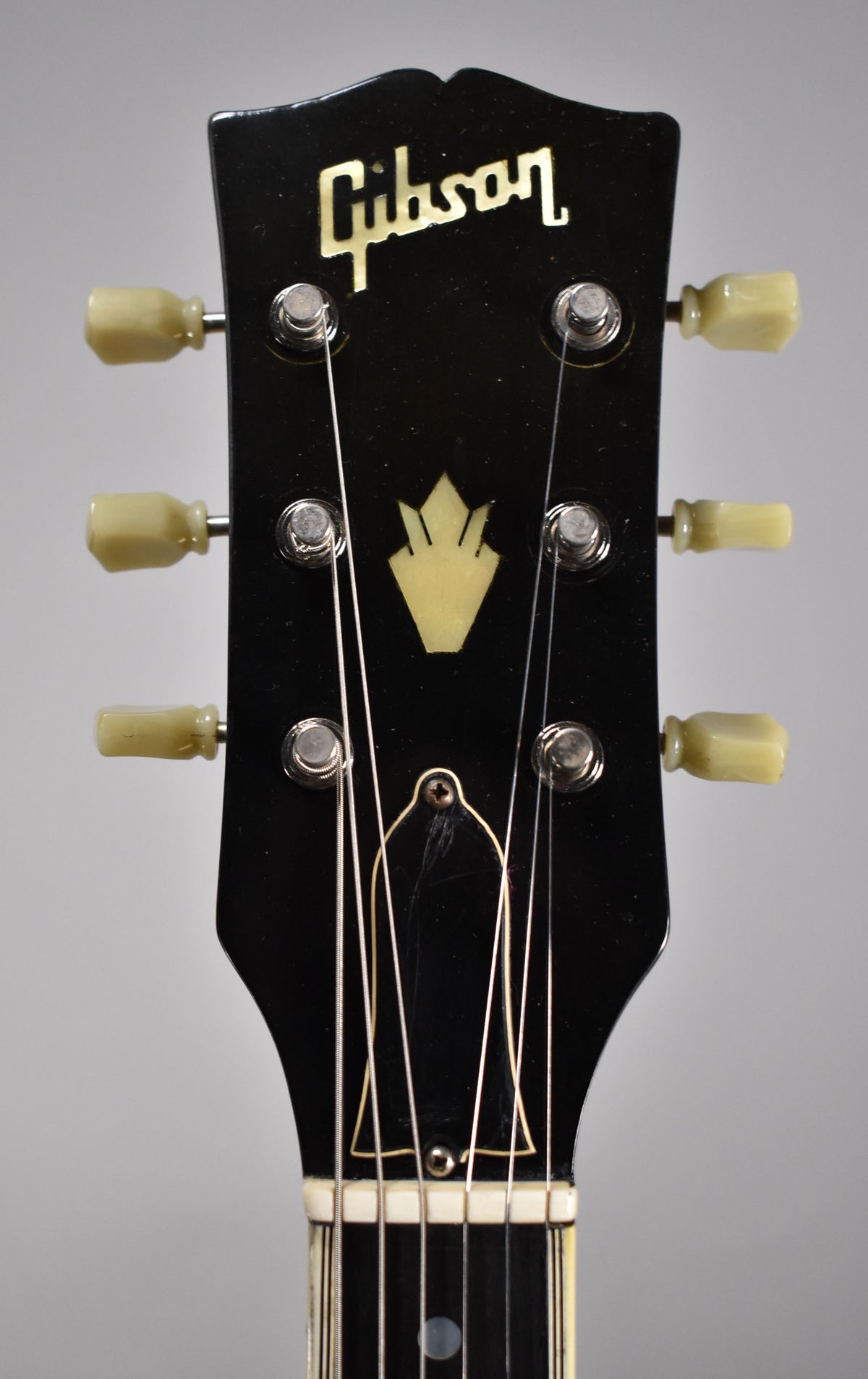 Close-up of the black headstock with a yellow crown inlay, six cream tuning pegs, and light wear around the truss rod cover.