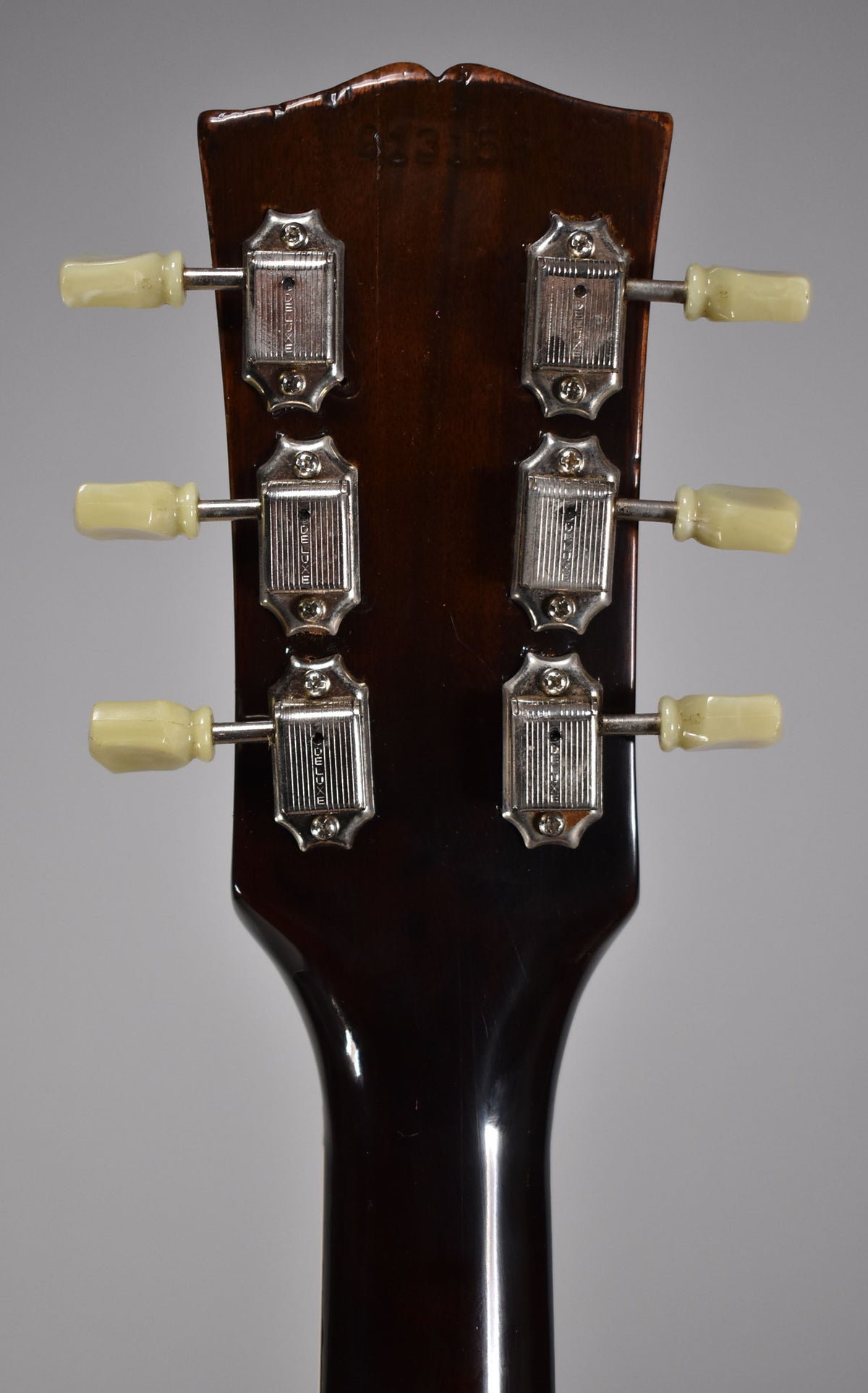 Rear view of the dark walnut headstock and neck, showing six chrome tuners with cream plastic buttons and some finish wear.
