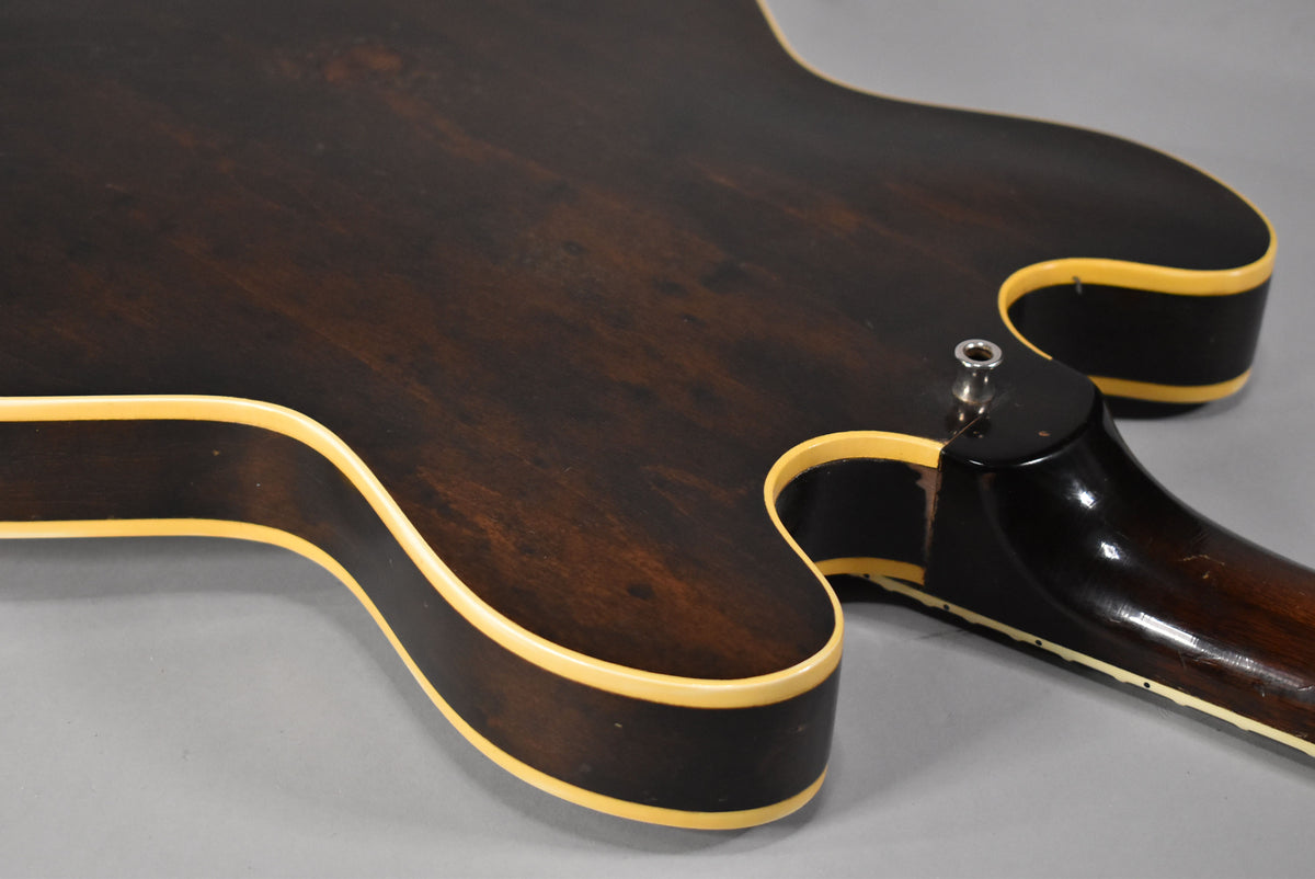 The back of a dark walnut hollow-body guitar, showing the neck joint, strap button, and cream binding along the body and neck.
