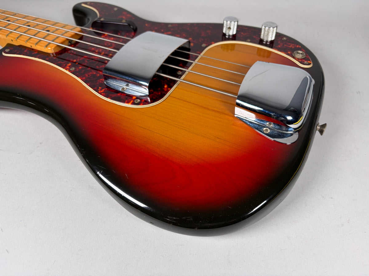 Close-up of the sunburst bass body, showing the chrome bridge cover, tortoise pickguard, and some scratches on the lower bout.