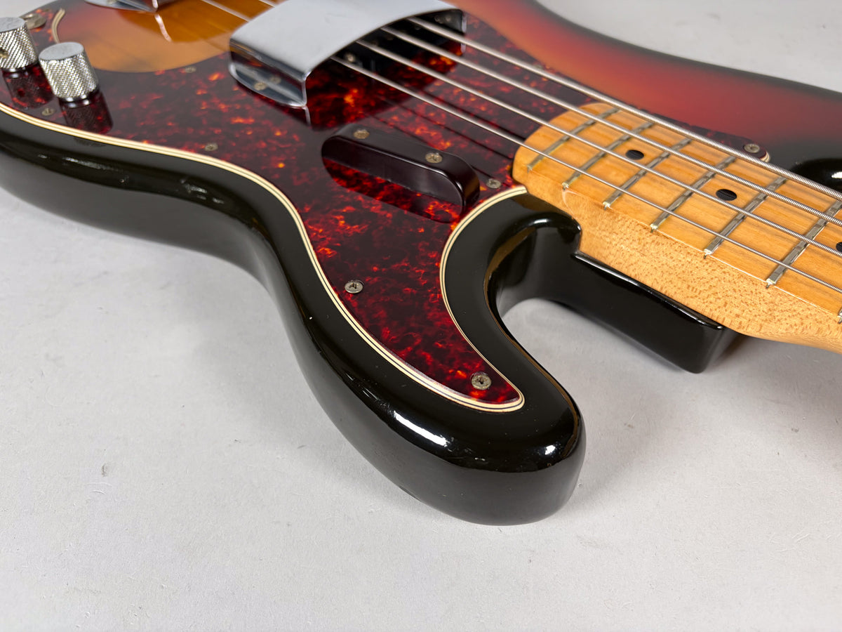 Upper body of a sunburst bass with a tortoiseshell pickguard, chrome bridge cover, and two knurled control knobs.