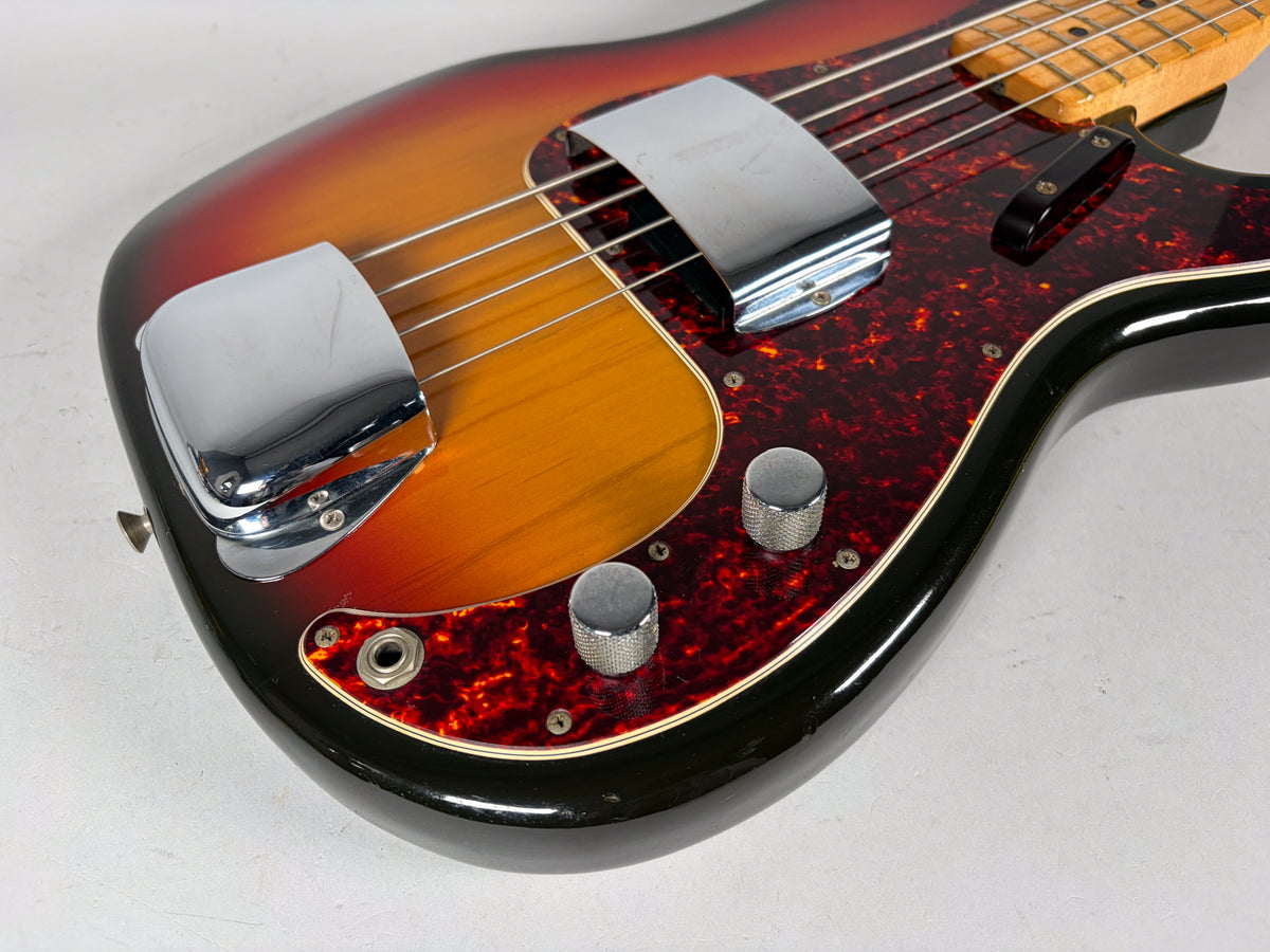 Close-up of the bass body, showing the sunburst finish, tortoiseshell pickguard, chrome bridge cover, and two knurled control knobs.