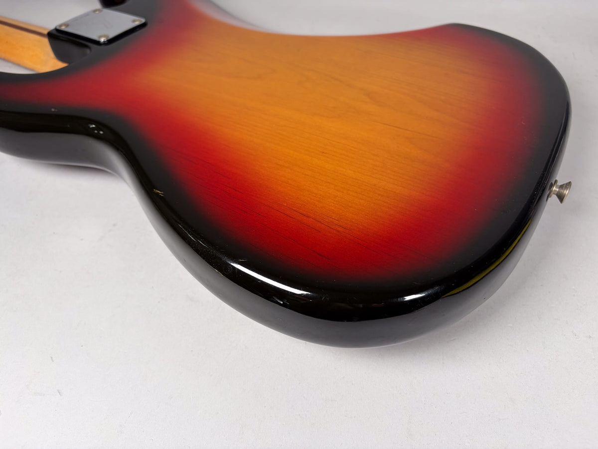 The bass guitar's sunburst body, viewed from the back, shows a glossy finish with minor dings and a strap button on the lower horn.