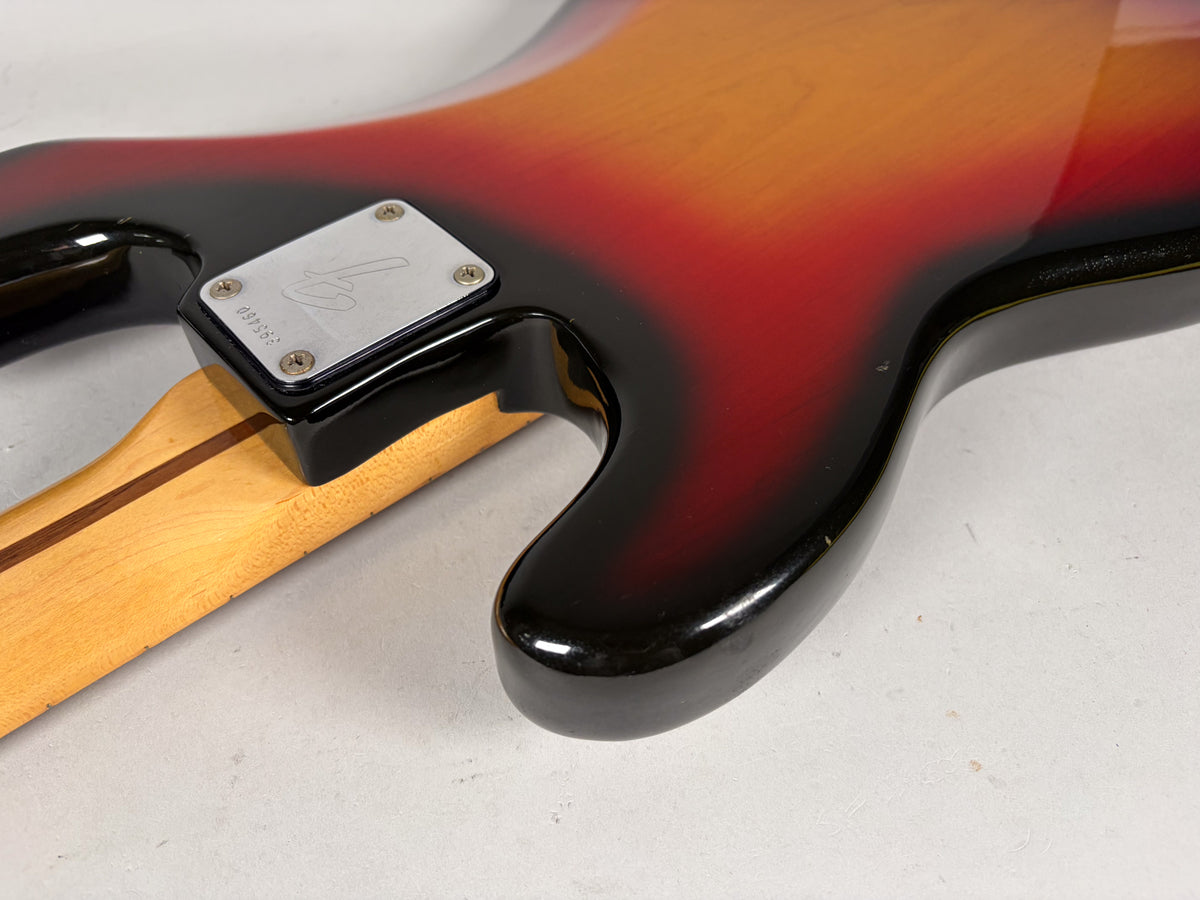 Close-up of the bass guitar's sunburst body and neck joint, showing a chrome neck plate and minor wear on the glossy finish.