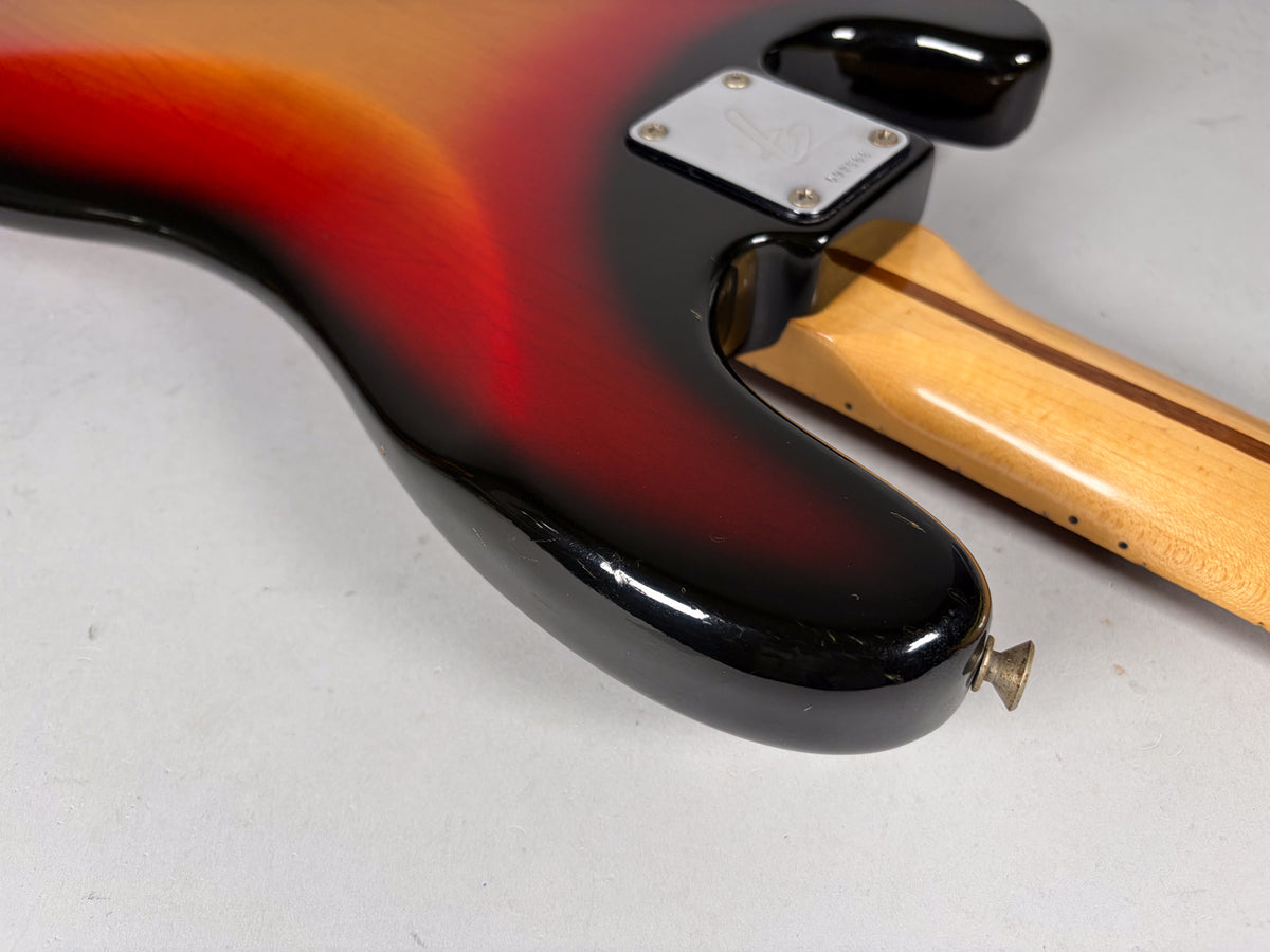 The bass body's lower horn and neck joint, showing the sunburst finish, a chrome neck plate, and a brass strap button.