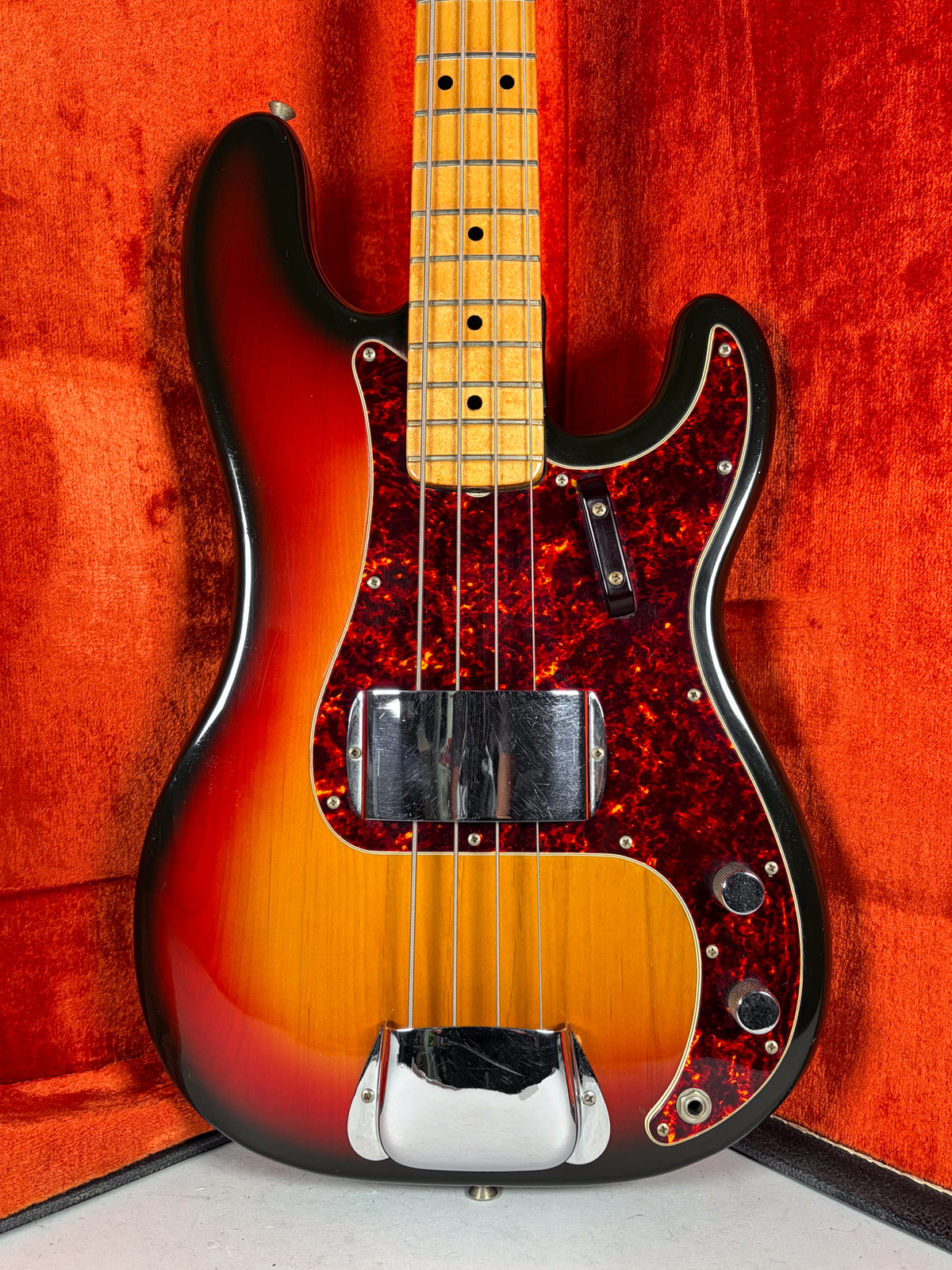 Full-body view of a sunburst bass with a tortoiseshell pickguard, chrome pickup cover, and bridge cover, showing light wear.