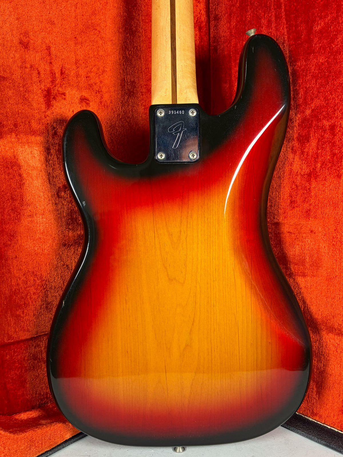 Rear view of the sunburst bass body, showing the neck plate with serial number and a few small dings on the black finish.