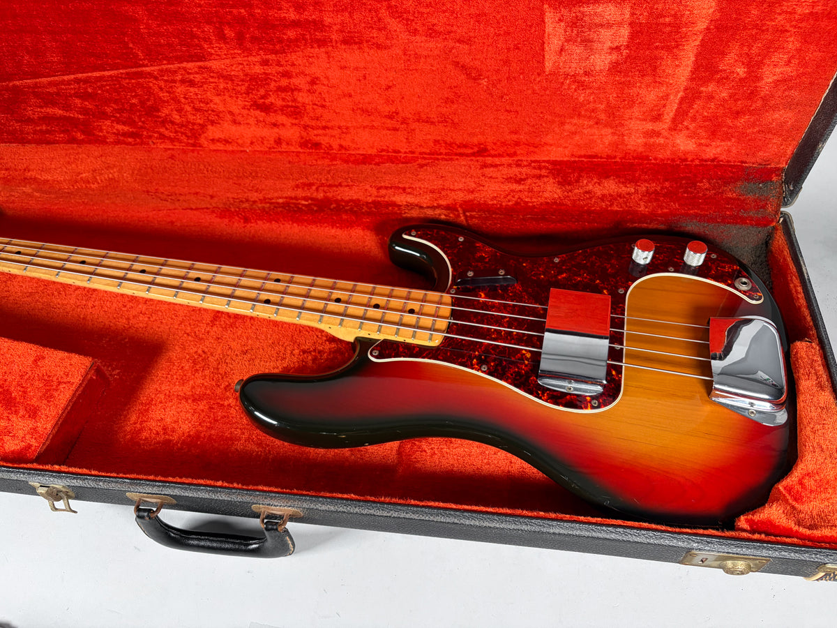 Sunburst bass in a red velvet case, showing a tortoiseshell pickguard, chrome bridge cover, and two control knobs.