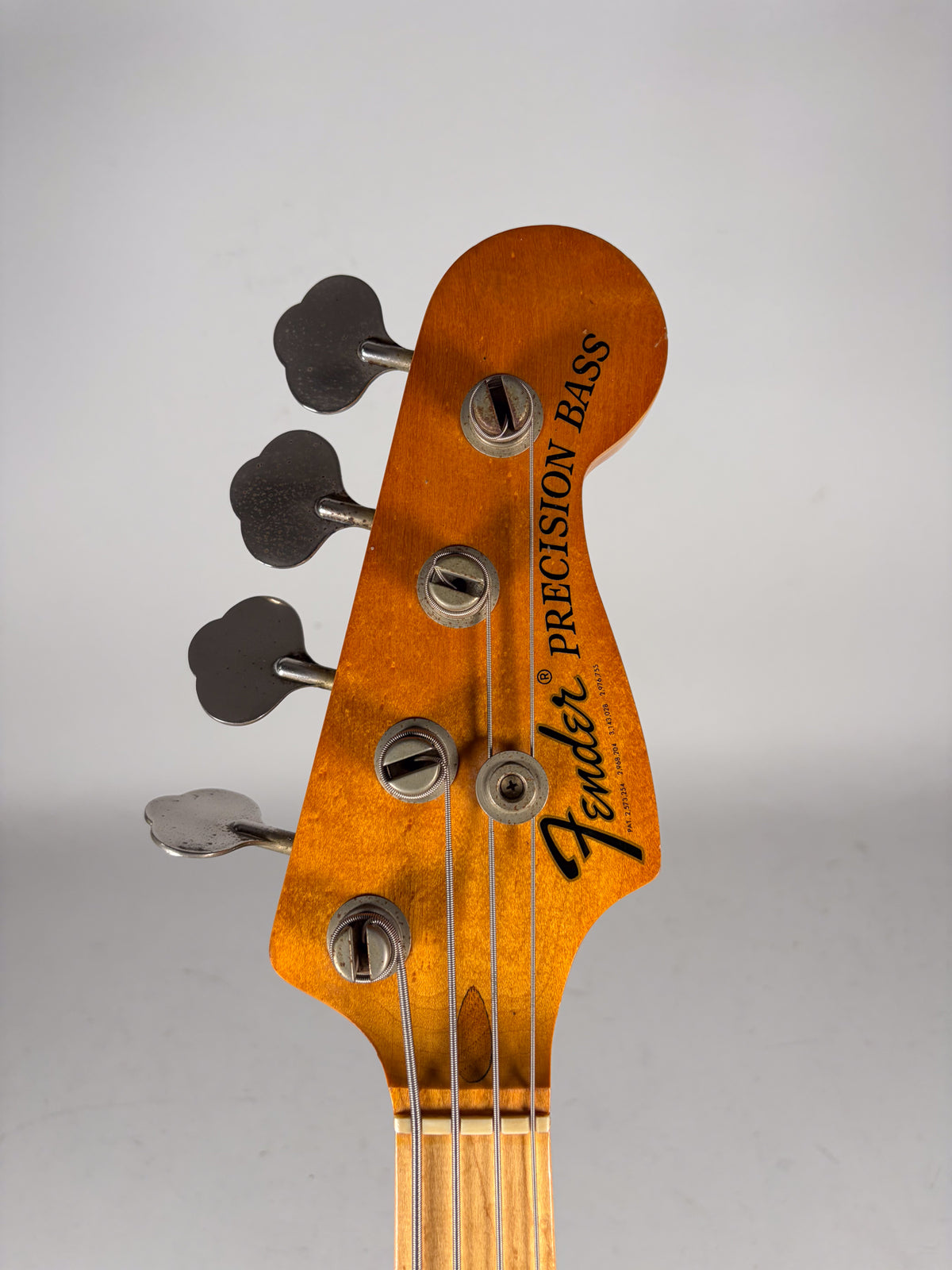 Close-up of the bass headstock, showing four clover-leaf tuners, string tree, and light wear on the amber finish.