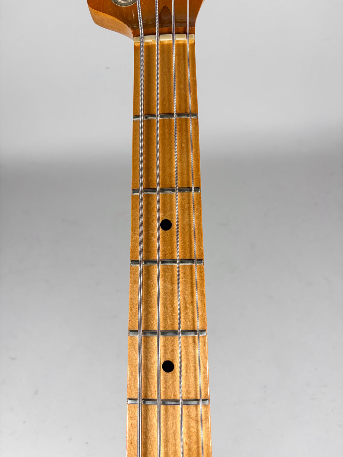 Close-up of the bass guitar's maple neck and fretboard, showing two black dot inlays and four strings over silver frets.