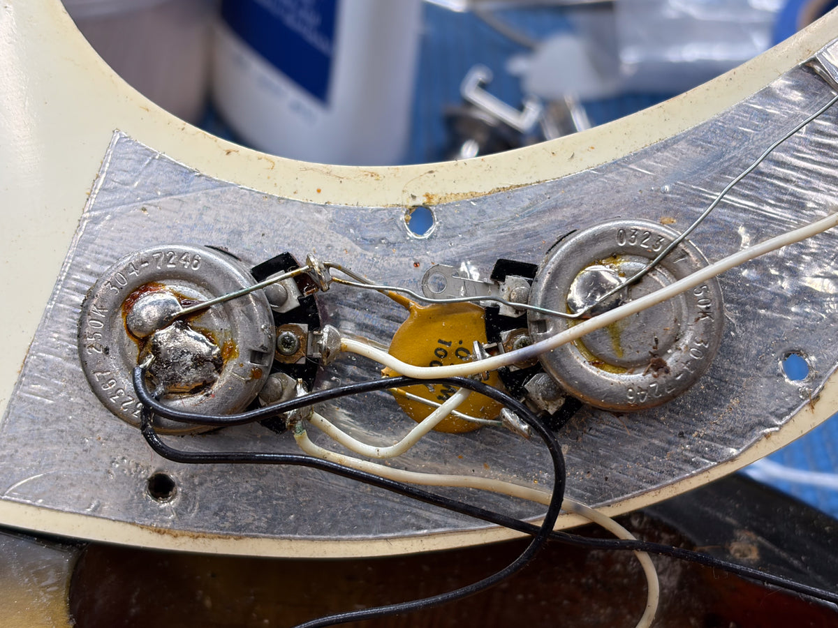 Close-up of the bass's electronics, showing two tarnished pots, a yellow capacitor, and wiring on a metal shield.