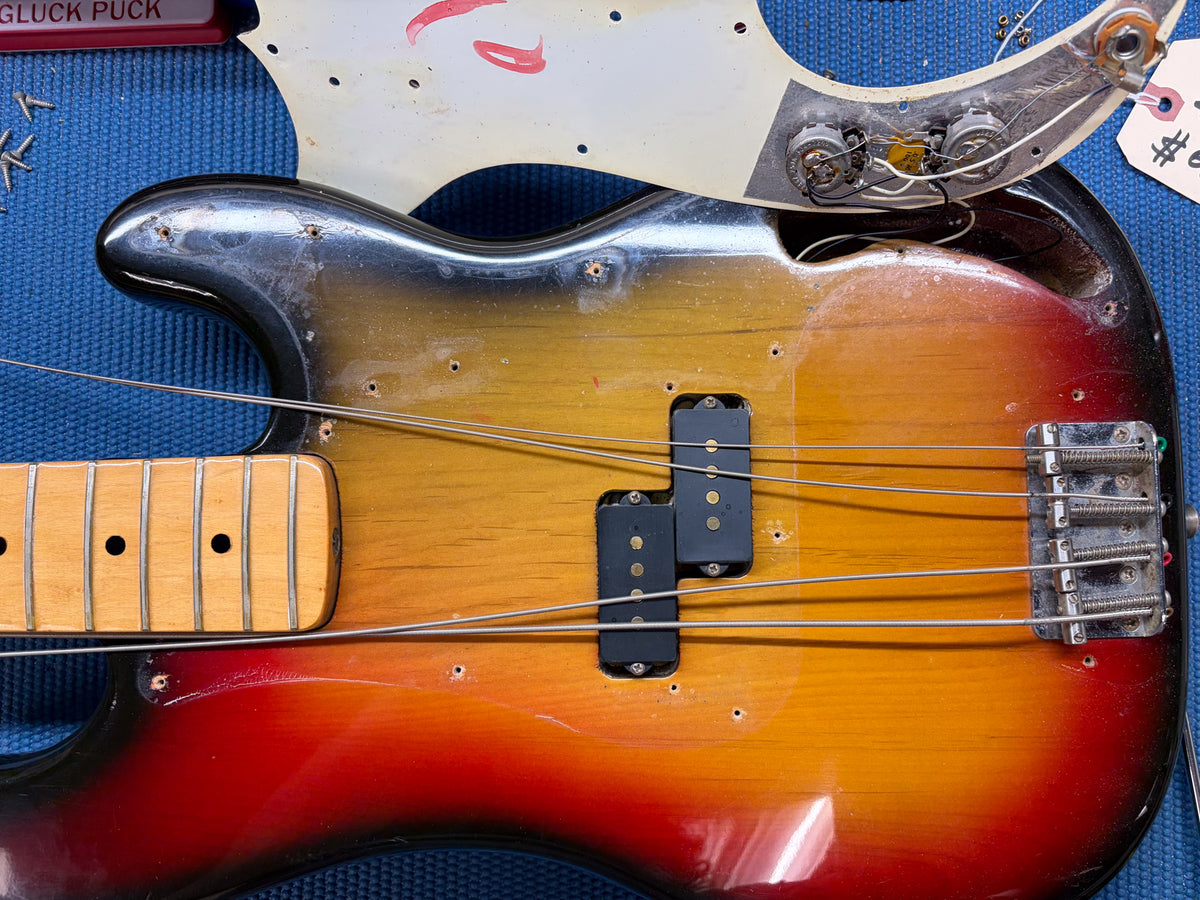 Close-up of the sunburst bass body, showing the split pickup, bridge, neck, and detached pickguard with wiring.