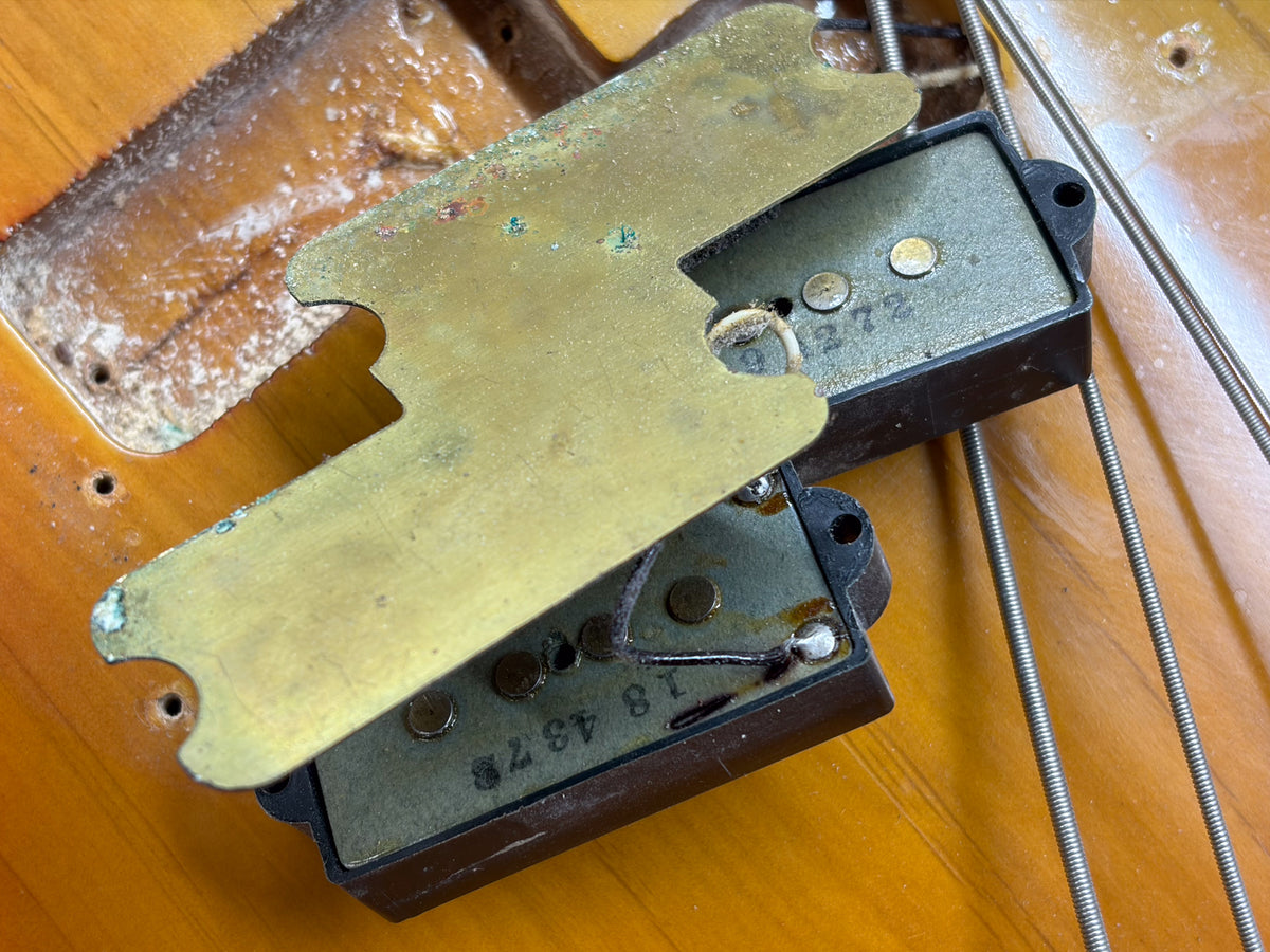 Close-up of the bass's split-coil pickup with its brass shielding plate removed, showing worn wiring and exposed pole pieces.