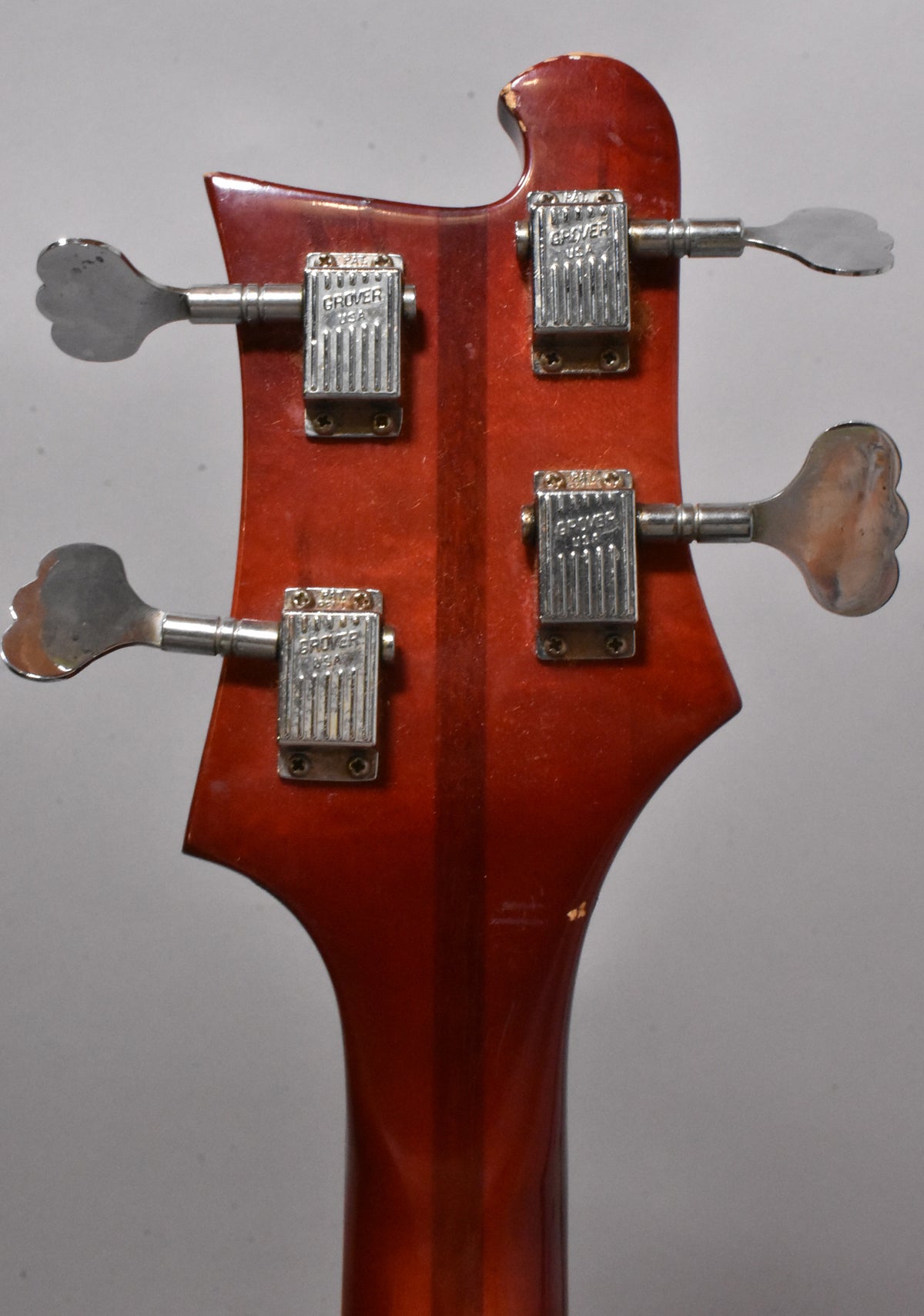 The bass's Fireglo headstock, with four chrome tuners and a worn finish, is viewed from the rear.